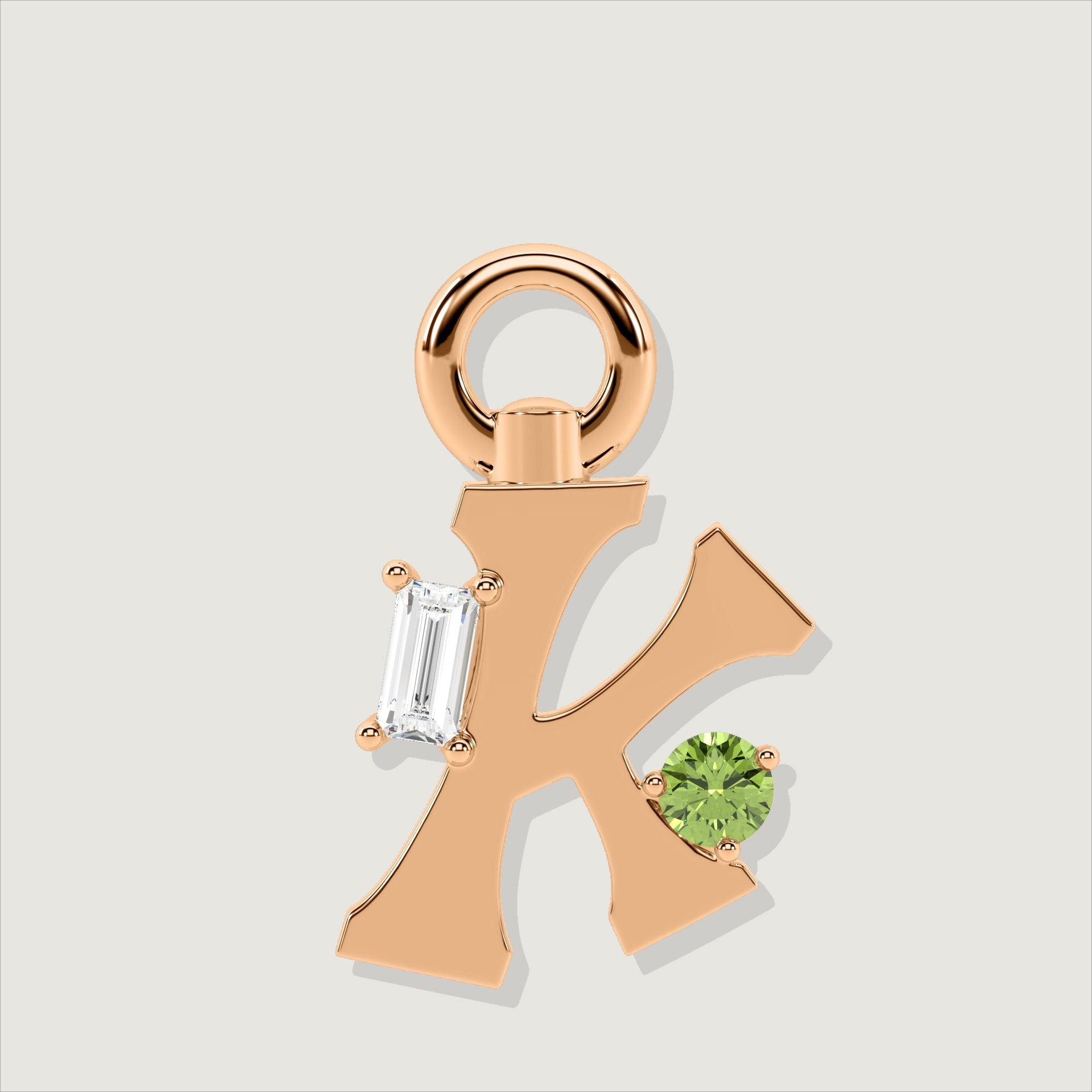 Rose gold letter K charm adorned with a baguette-cut clear stone and a round green gemstone.