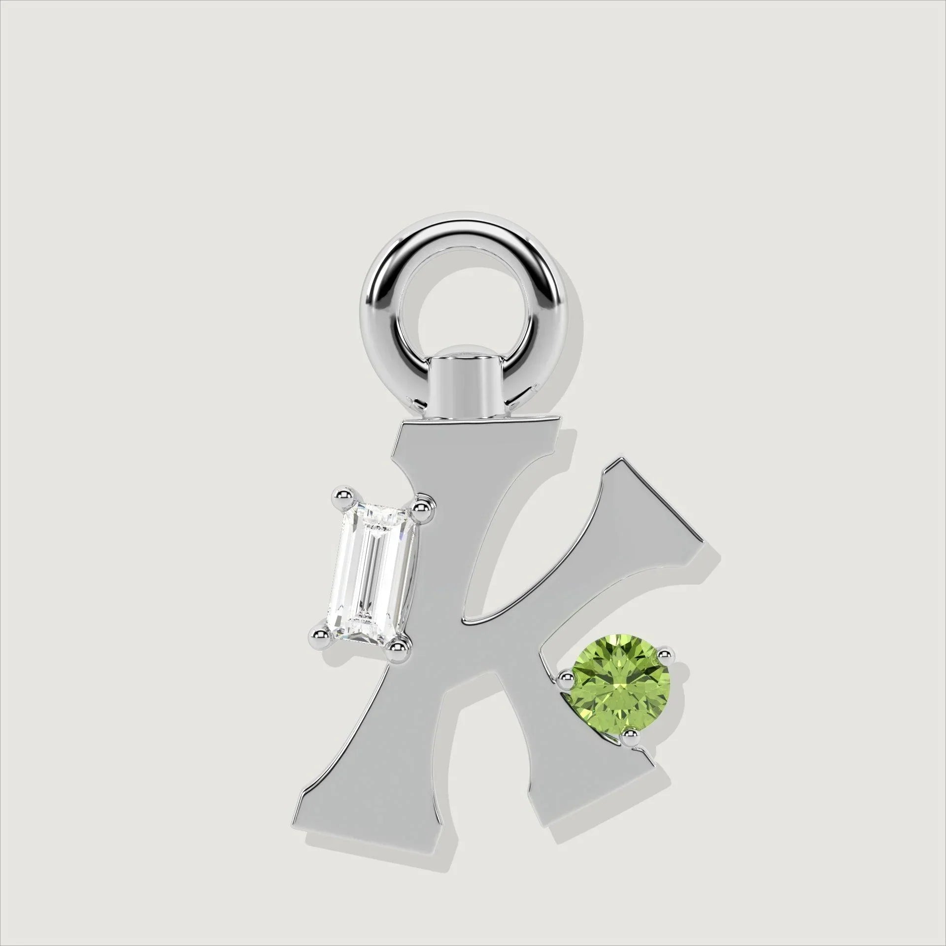 Silver letter K charm adorned with a baguette-cut clear stone and a round green gemstone.
