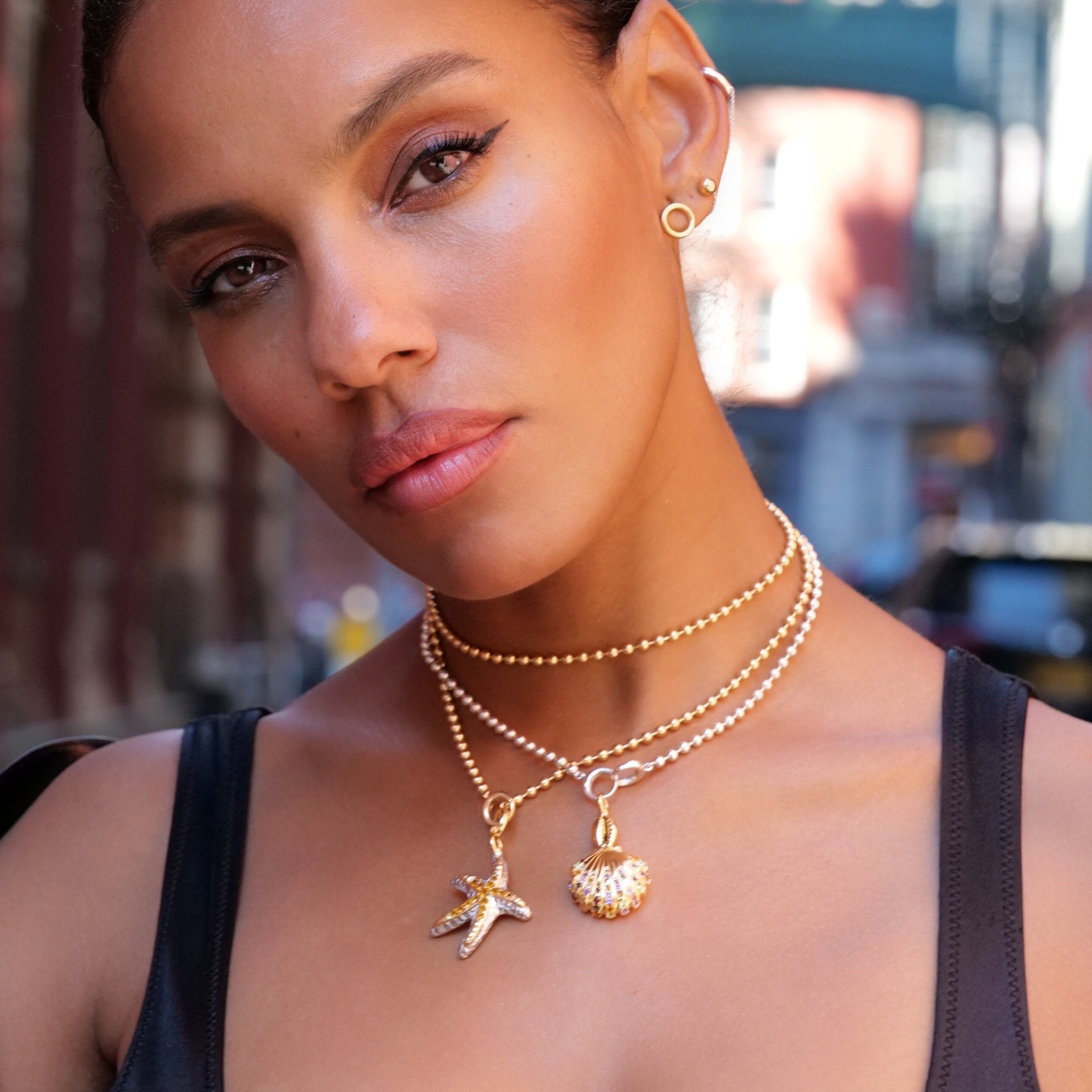 Woman wearing layered gold necklaces with starfish and seashell charms