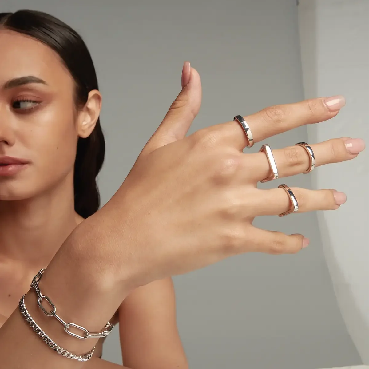 Model’s hand wearing multiple silver rings with geometric shapes, paired with chain bracelets.