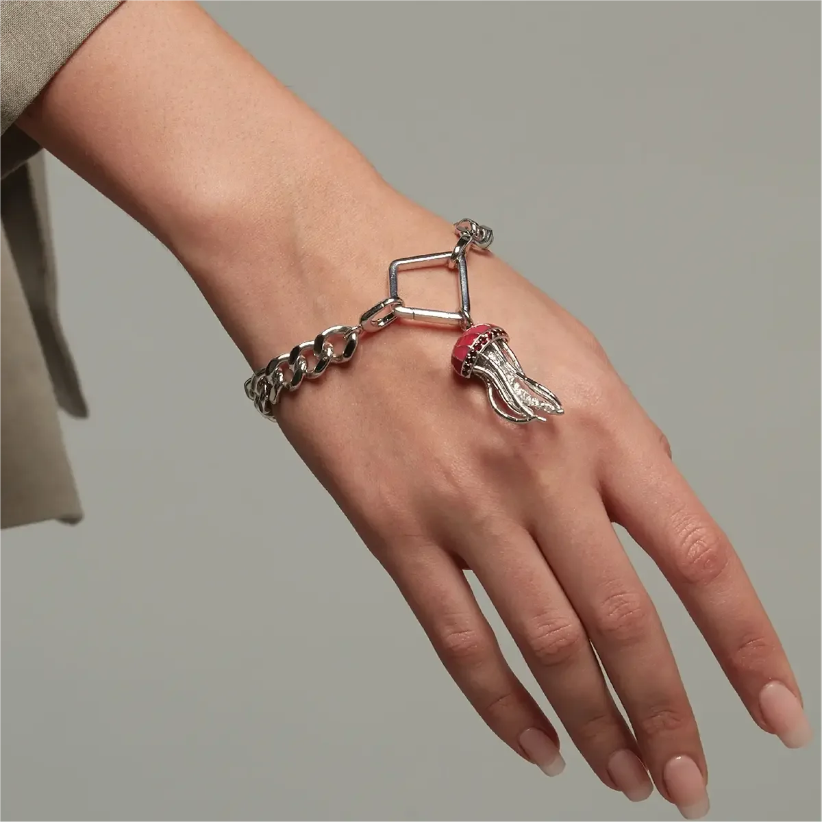 Close-up of a wrist wearing a chunky silver chain bracelet with a geometric connector and a dangling jellyfish charm.