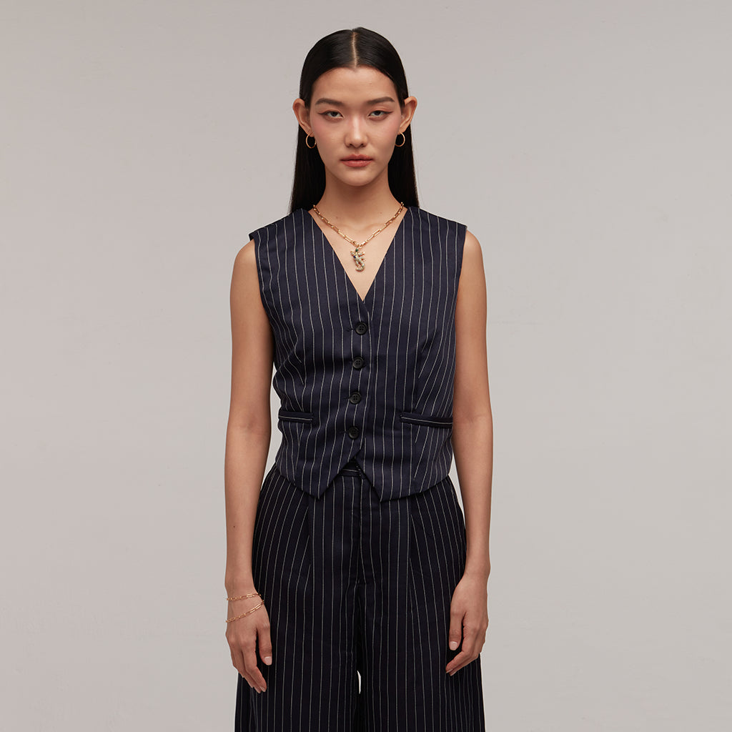 Woman in navy pinstripe vest and wide-leg trousers wearing statement gold lizard charm necklace