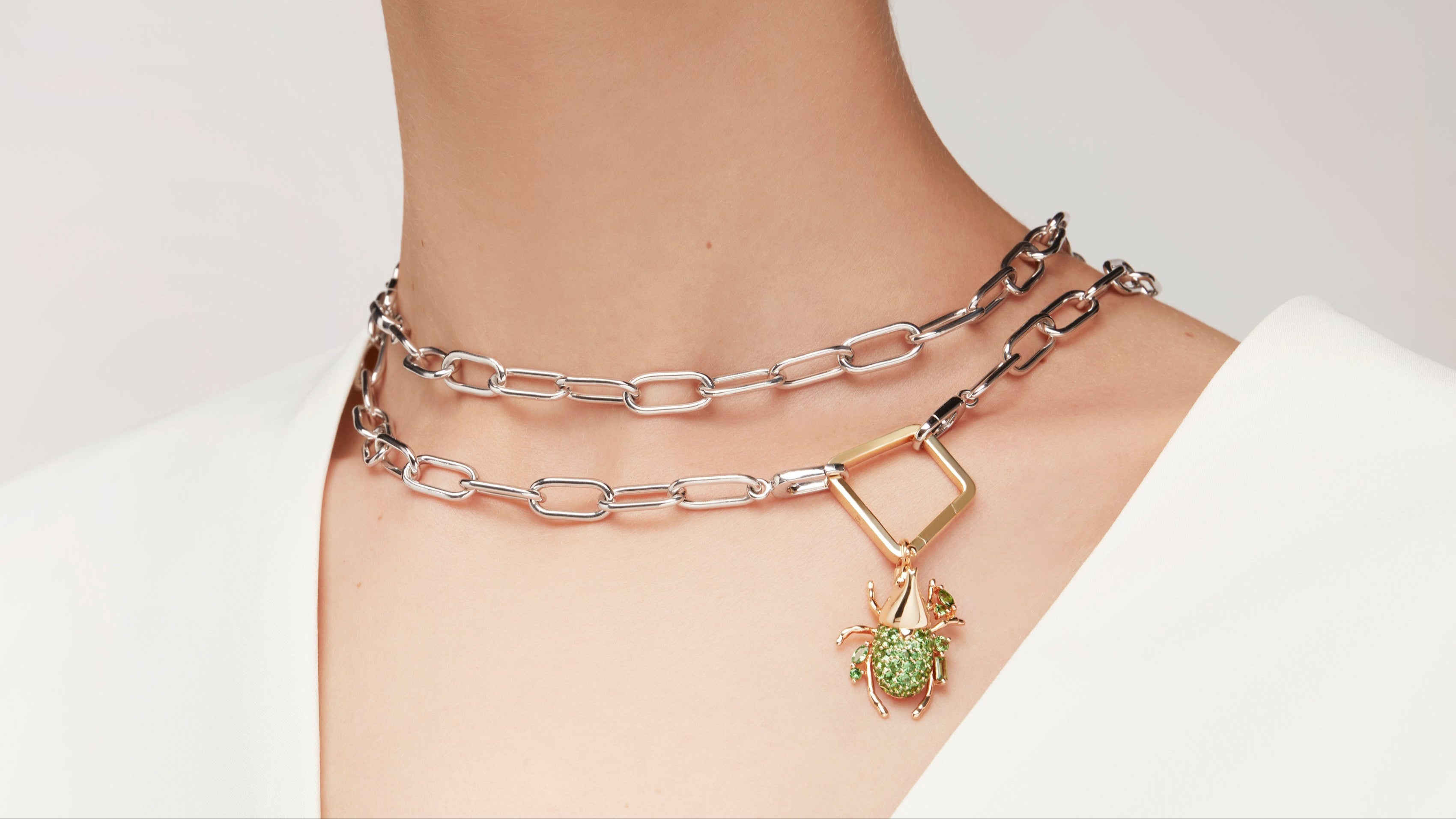 Layered silver chain necklace featuring gold-framed green gemstone beetle pendant.