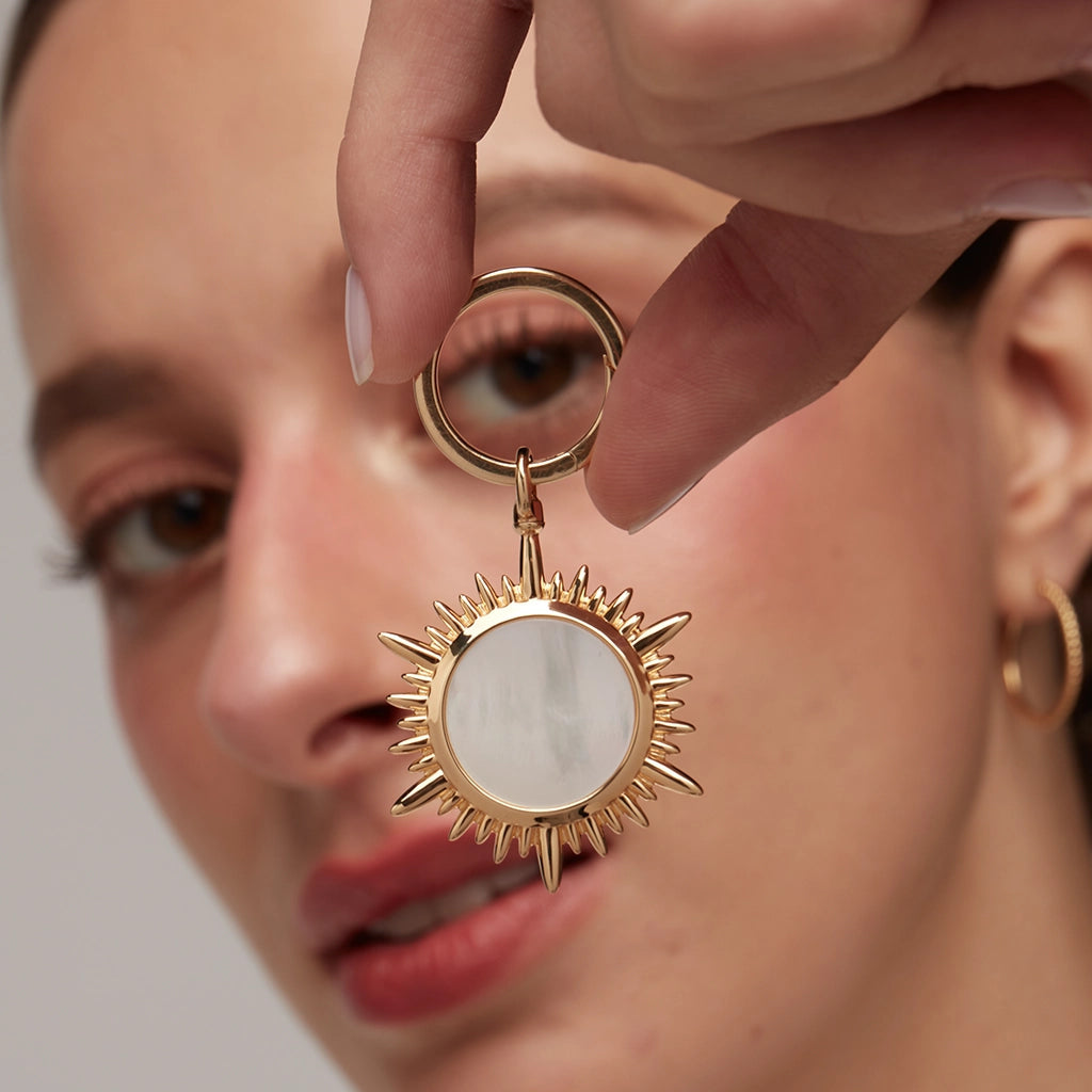 Gold sunburst charm with mother-of-pearl center held in hand, modern luxury jewelry.