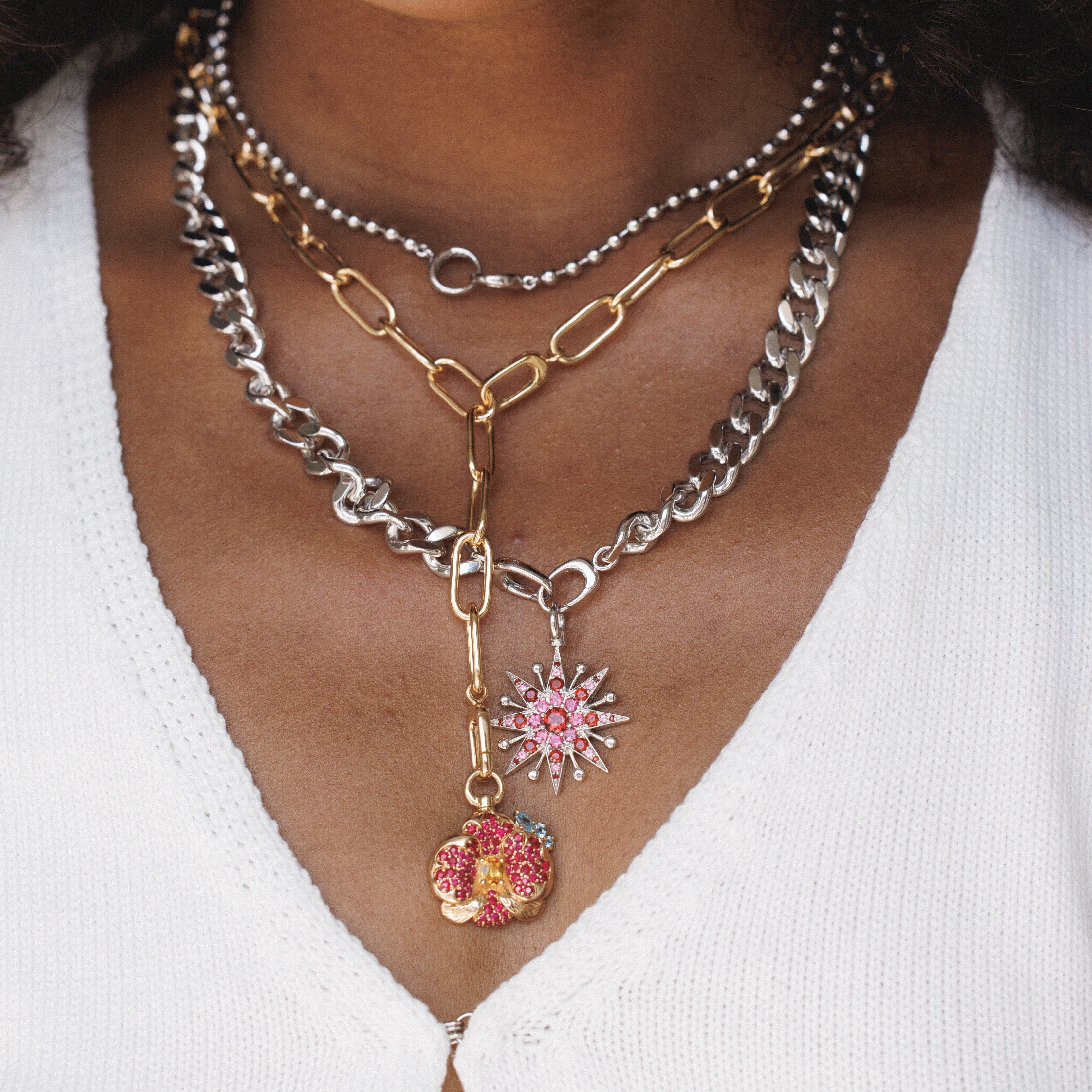 Layered gold and silver chain necklaces with pink flower and starburst charms.