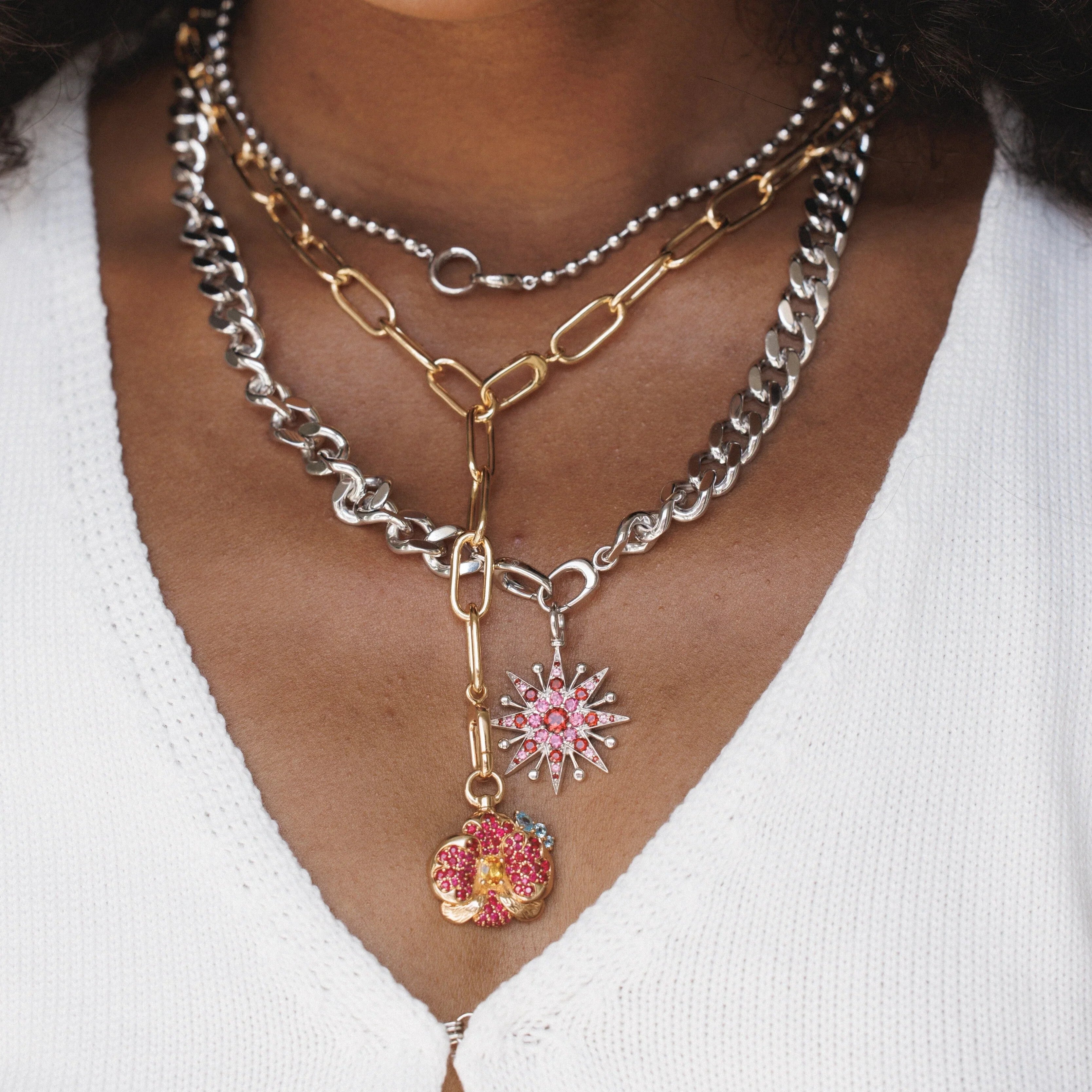 Layered gold and silver chain necklaces with pink flower and starburst charms.