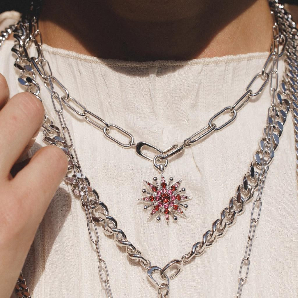 Layered silver link chain necklaces with ruby starburst charm on white top