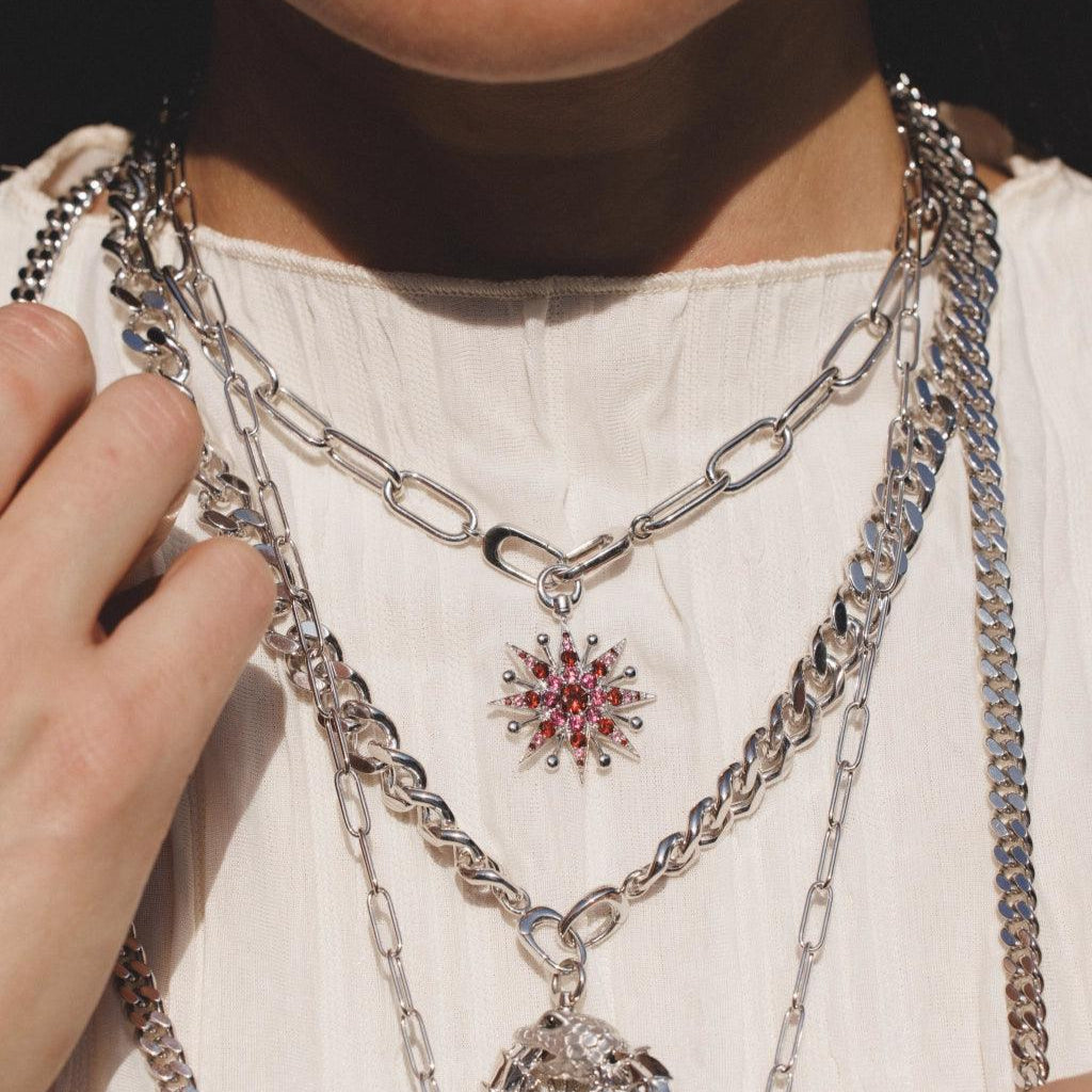 Layered silver chain necklaces with starburst and dragon charms on white blouse