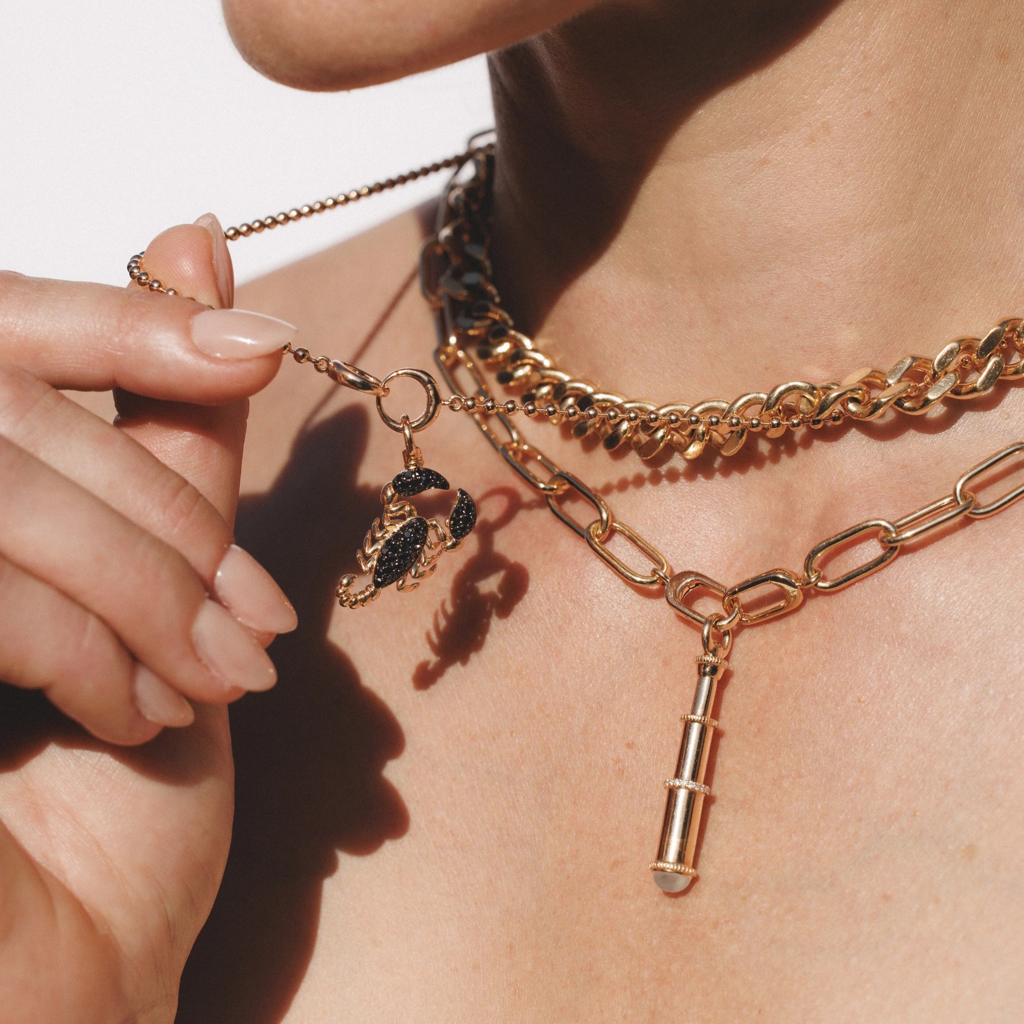 Layered gold necklaces with scorpion and telescope charms on a woman's neck.