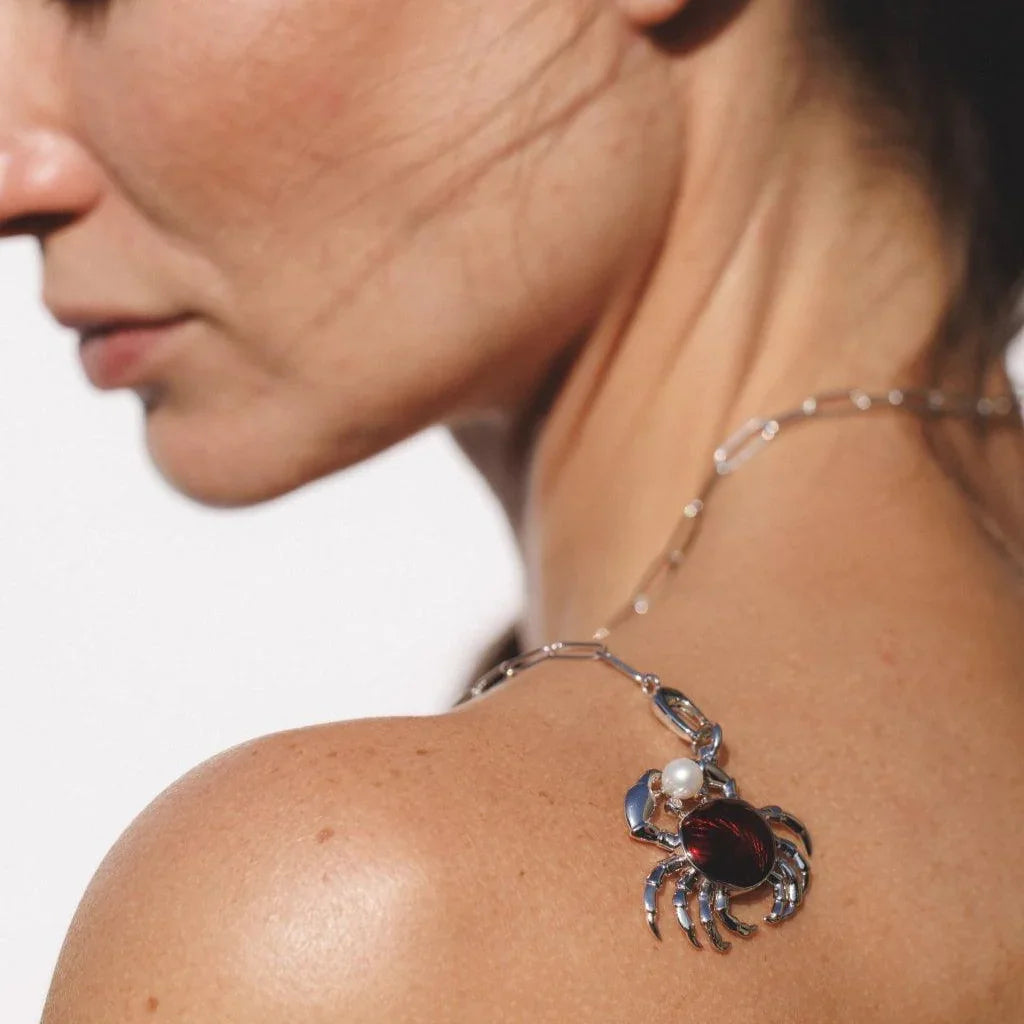 Artistic shot of red crab charm necklace styled across model's shoulder with pearl detail.