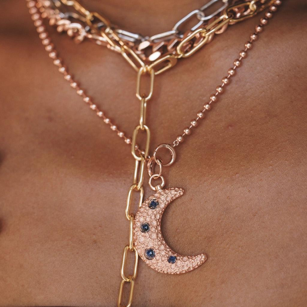 Textured gold moon charm pendant with blue stones on layered chain necklace