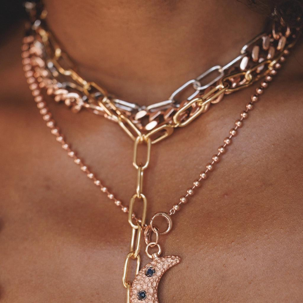 Layered gold and rose gold link chains with crescent moon charm set with blue gemstones.