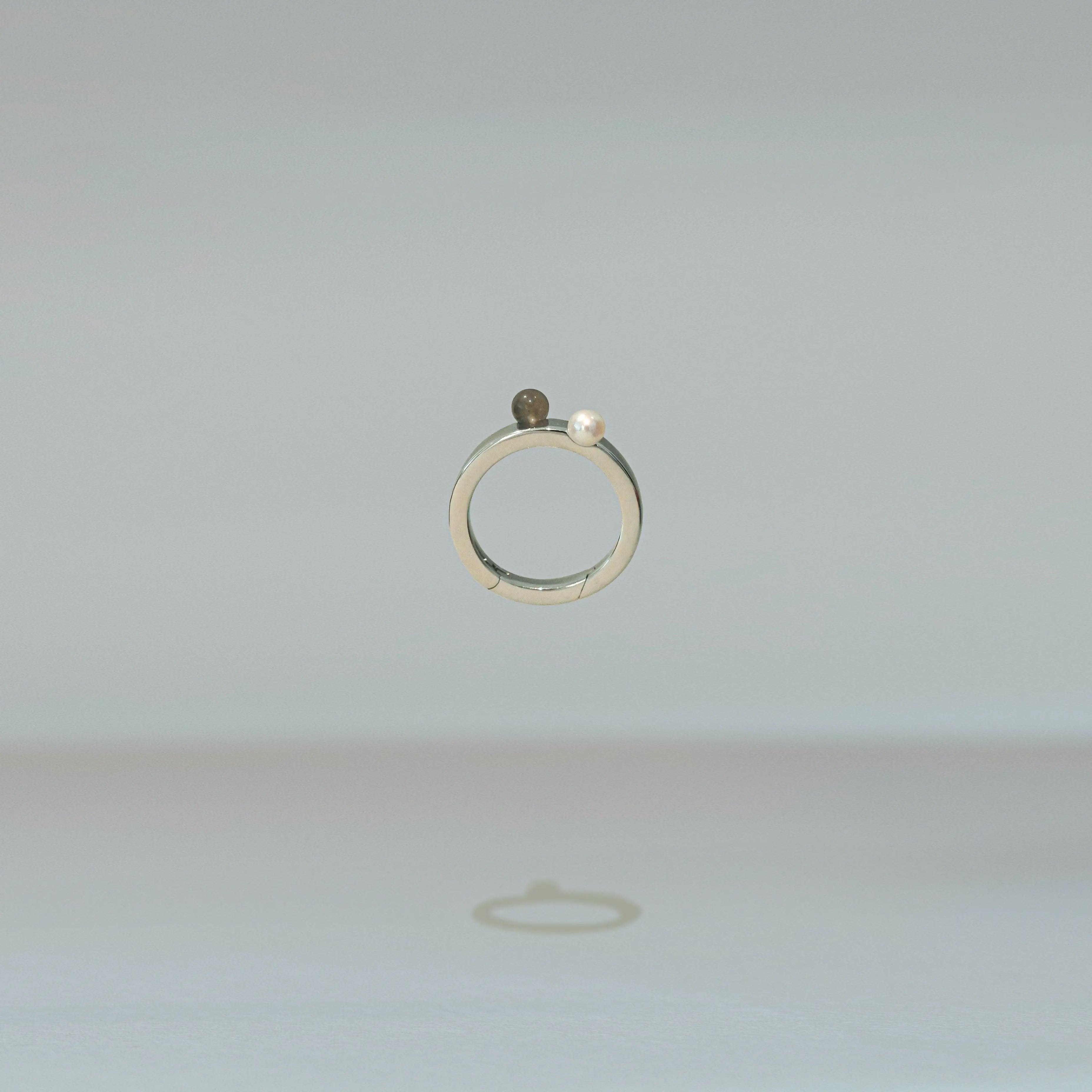 Silver ring with a pearl and small stone on a light gray background