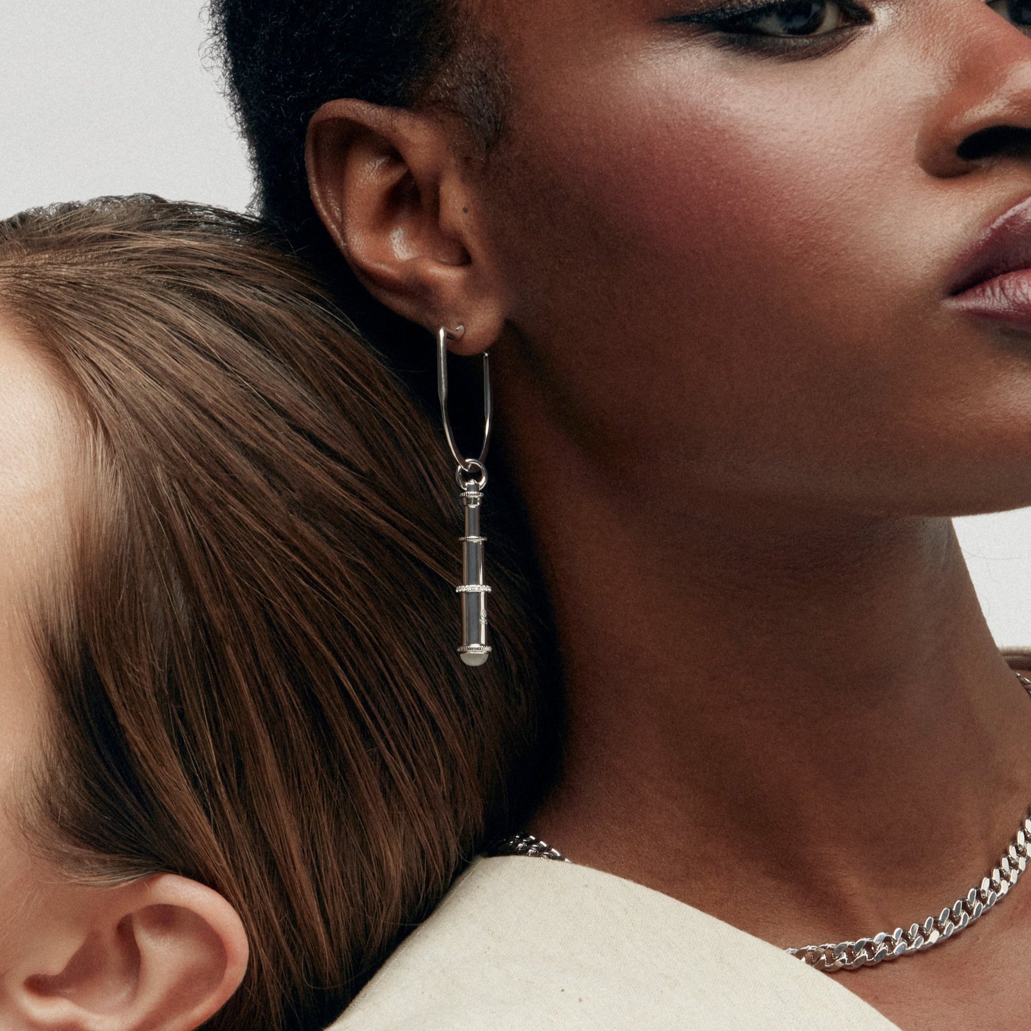 Two women wearing statement earrings, one with silver telescope drop earring.