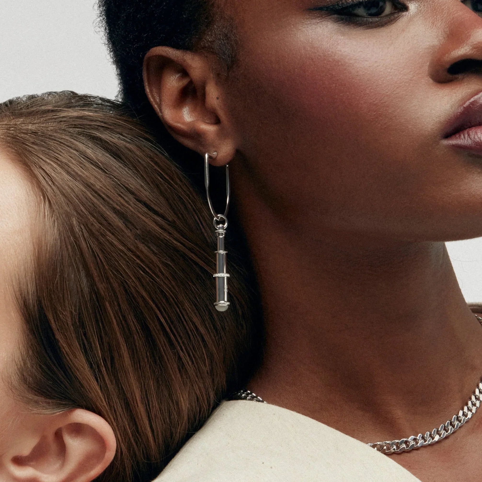 Two women wearing statement earrings, one with silver telescope drop earring.