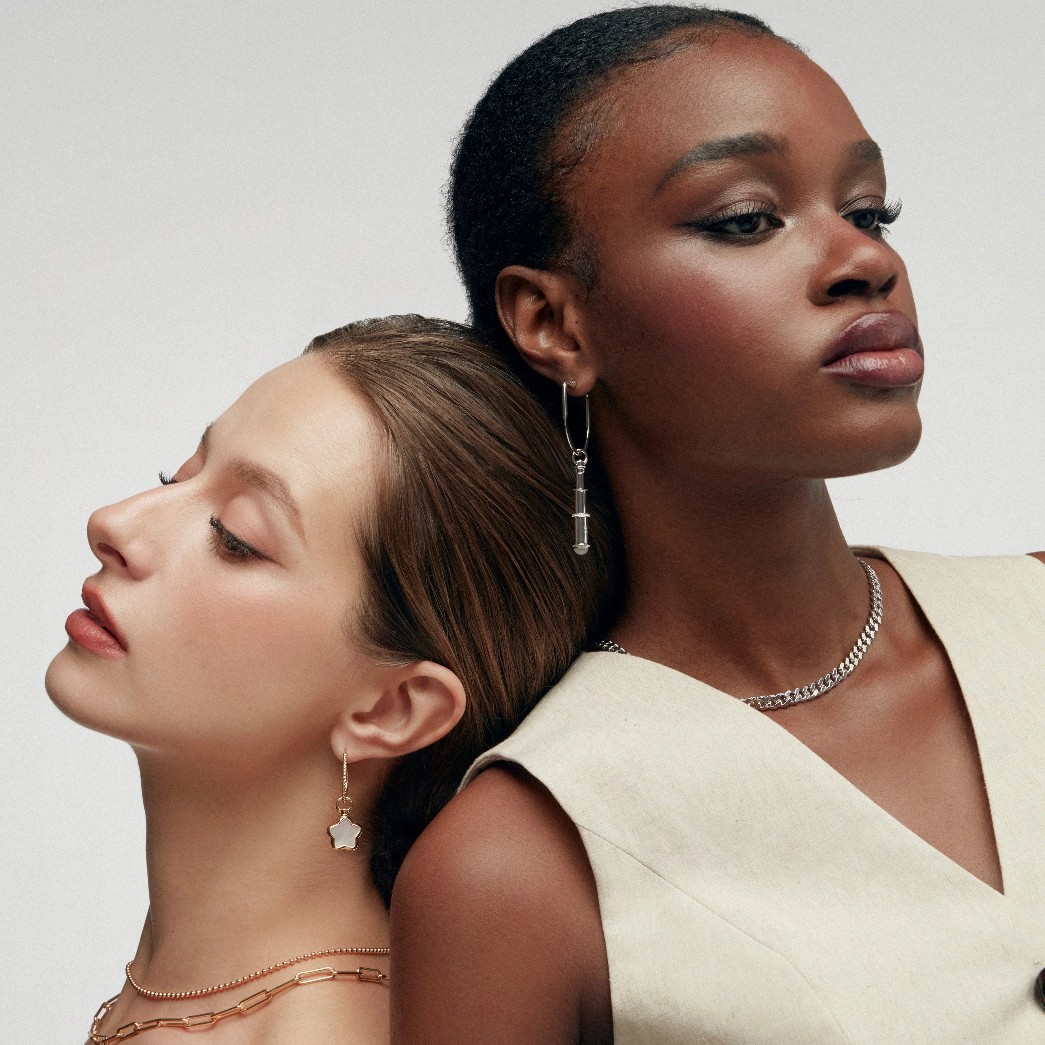 Two women wearing silver telescope and star-shaped mother of pearl earrings styled with delicate chain necklaces.