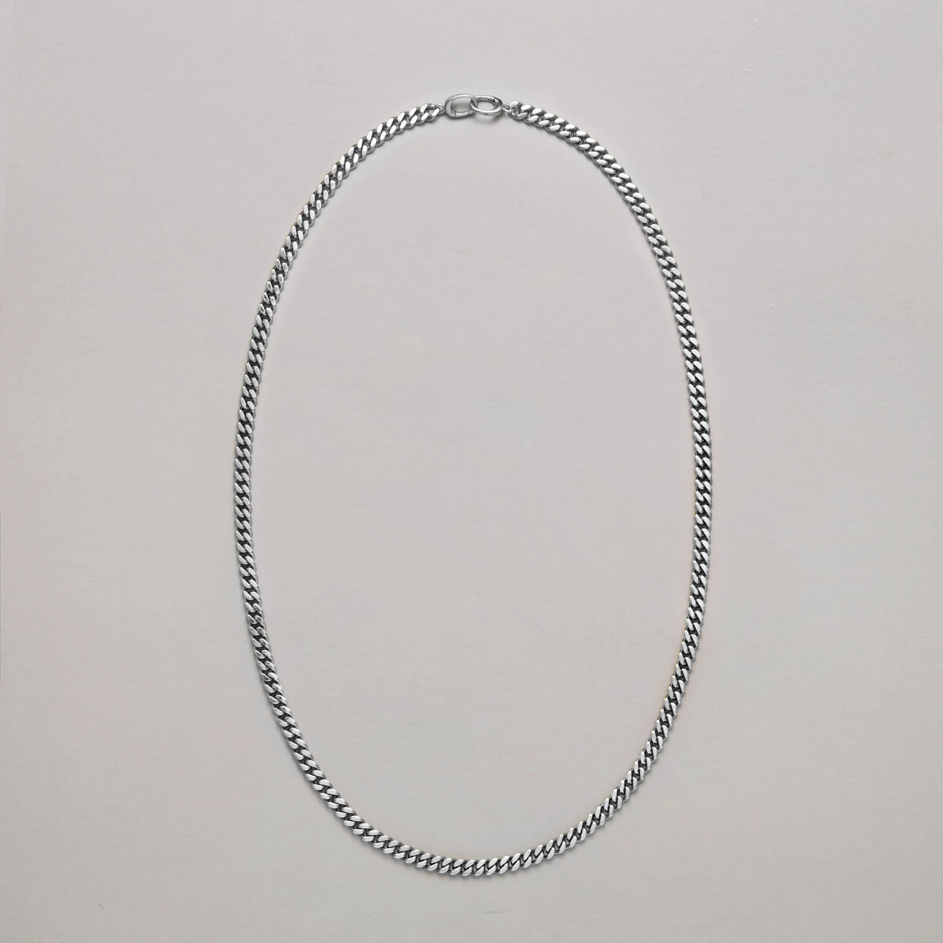 Silver curb chain necklace displayed on neutral background.