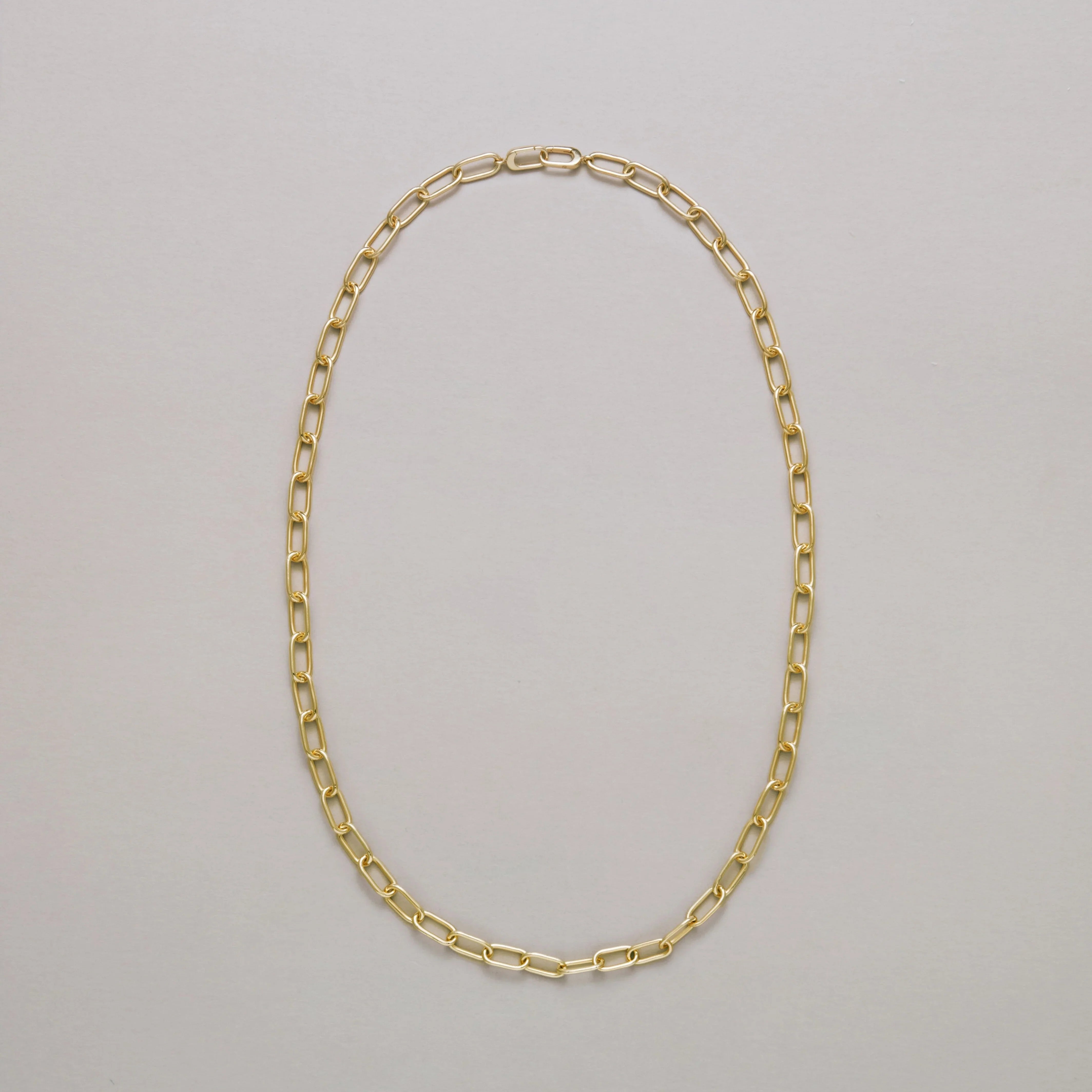 Long gold paperclip chain necklace on a light gray background