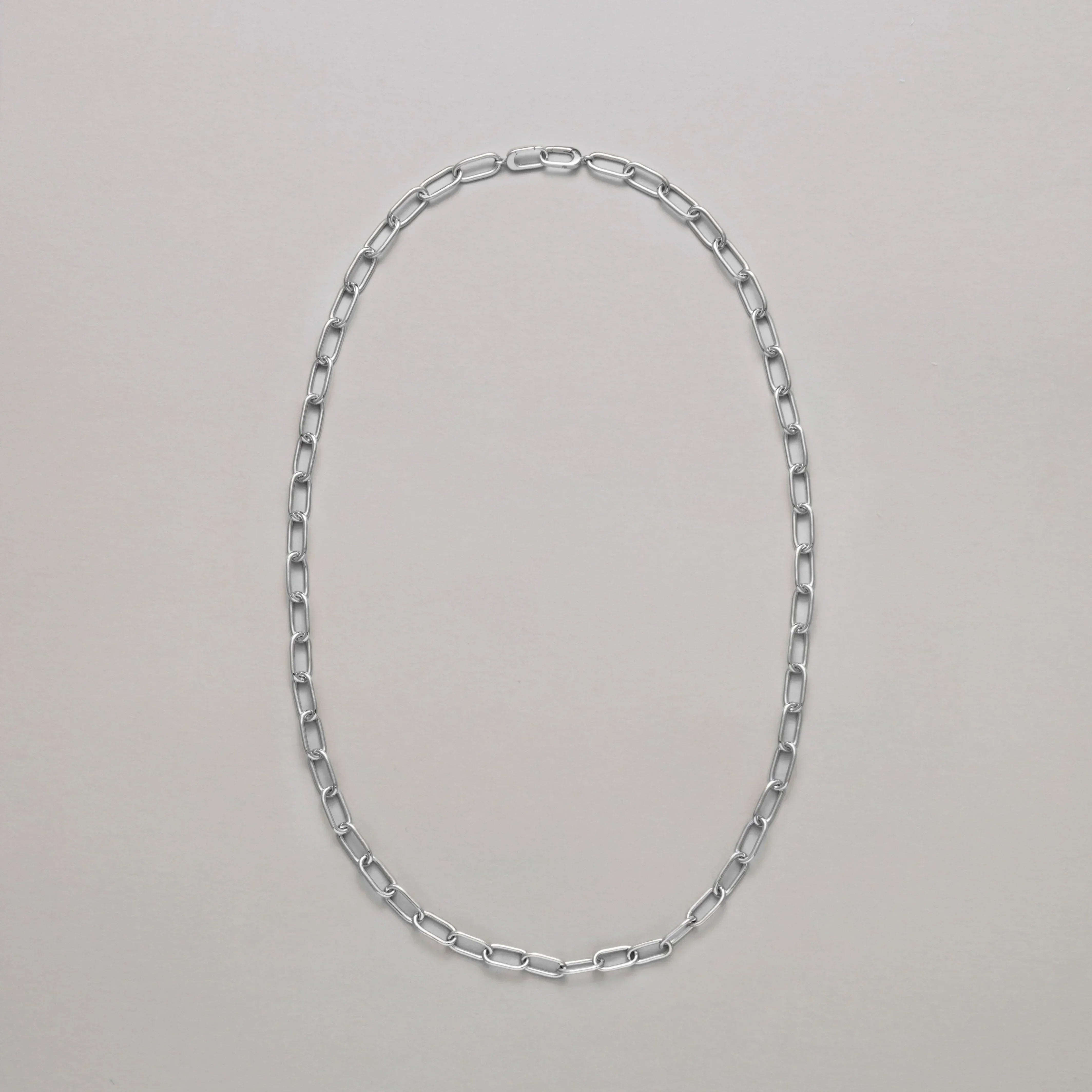 Long silver paperclip chain necklace on a light gray background