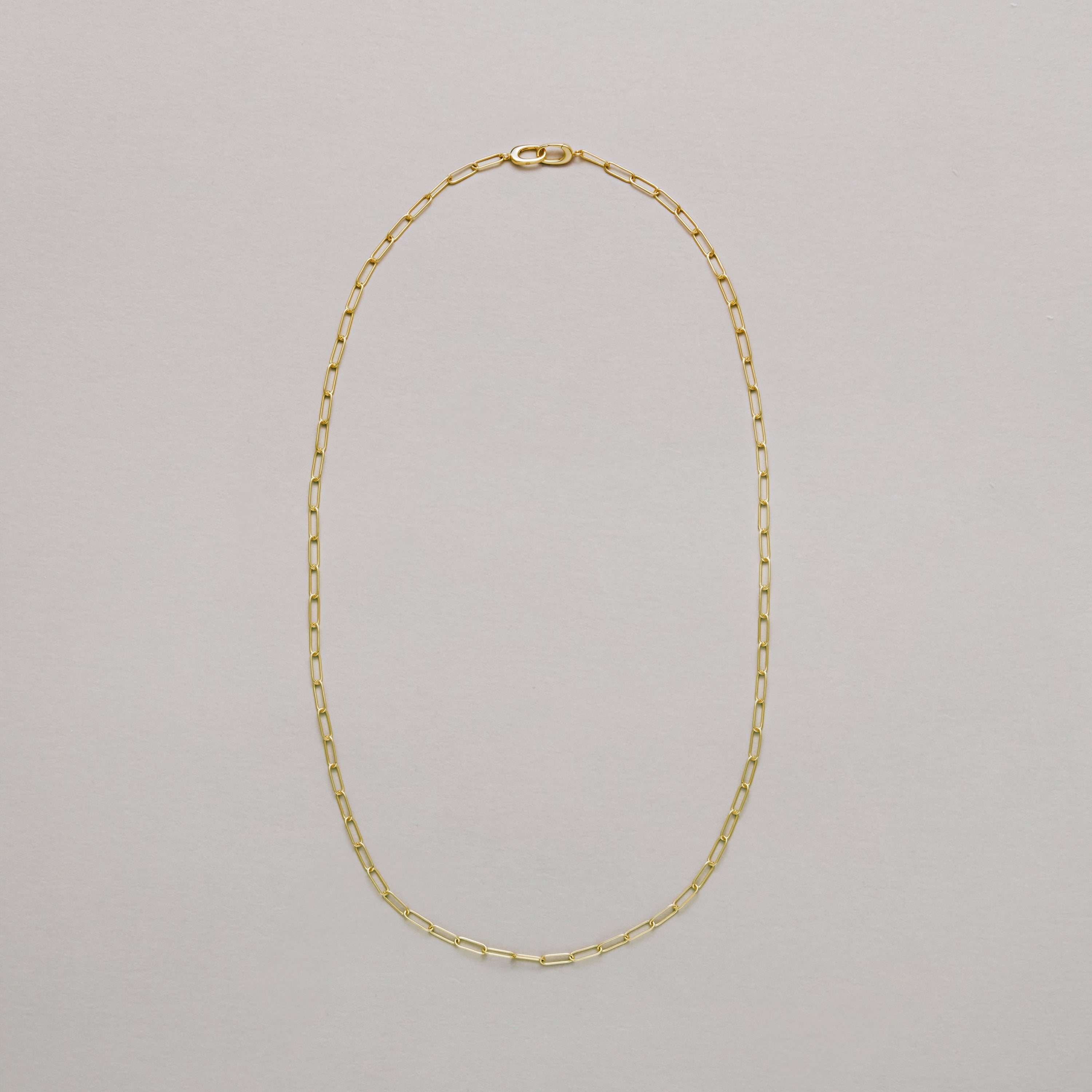 Long gold paperclip chain necklace on a light gray background