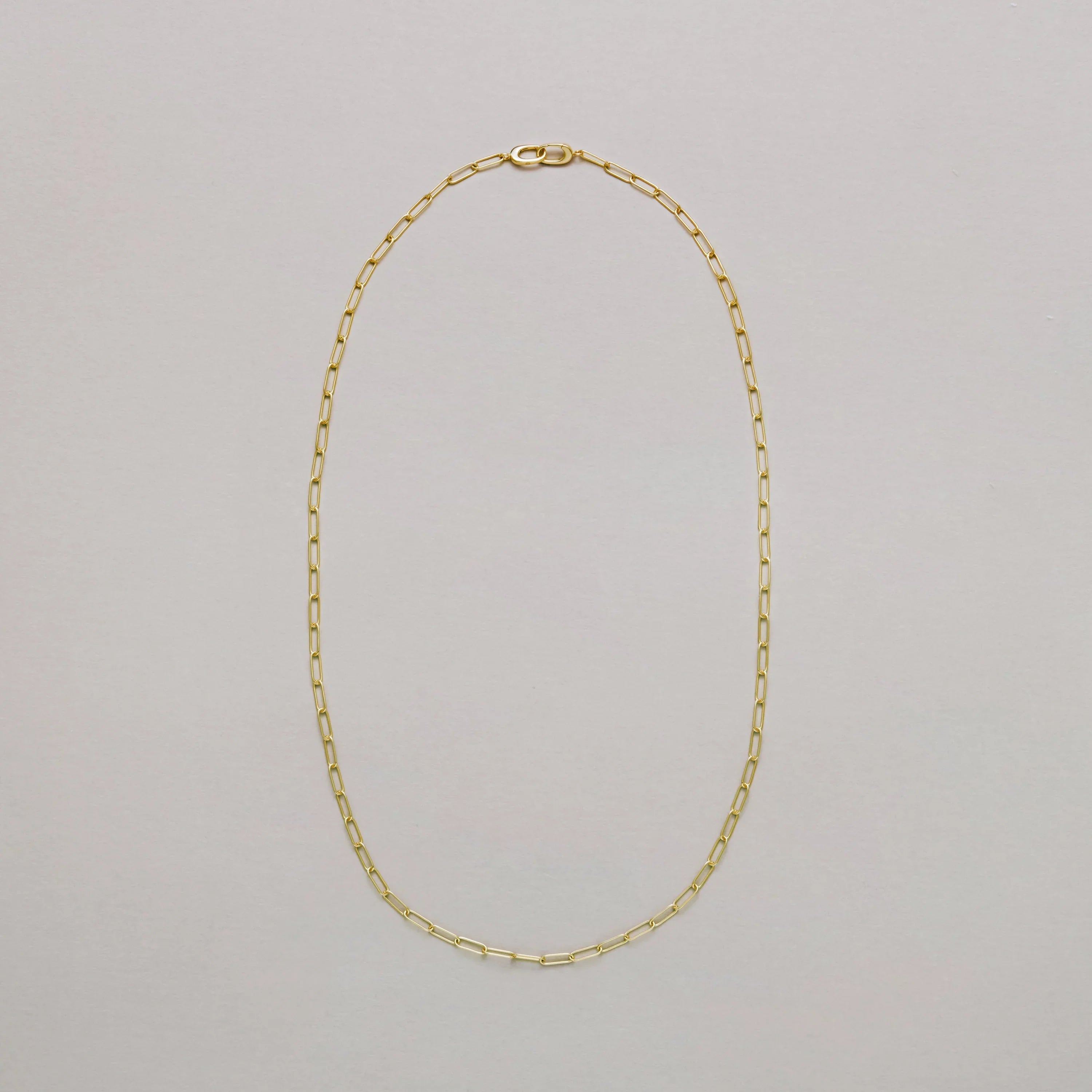 Gold paperclip chain necklace on a light gray background