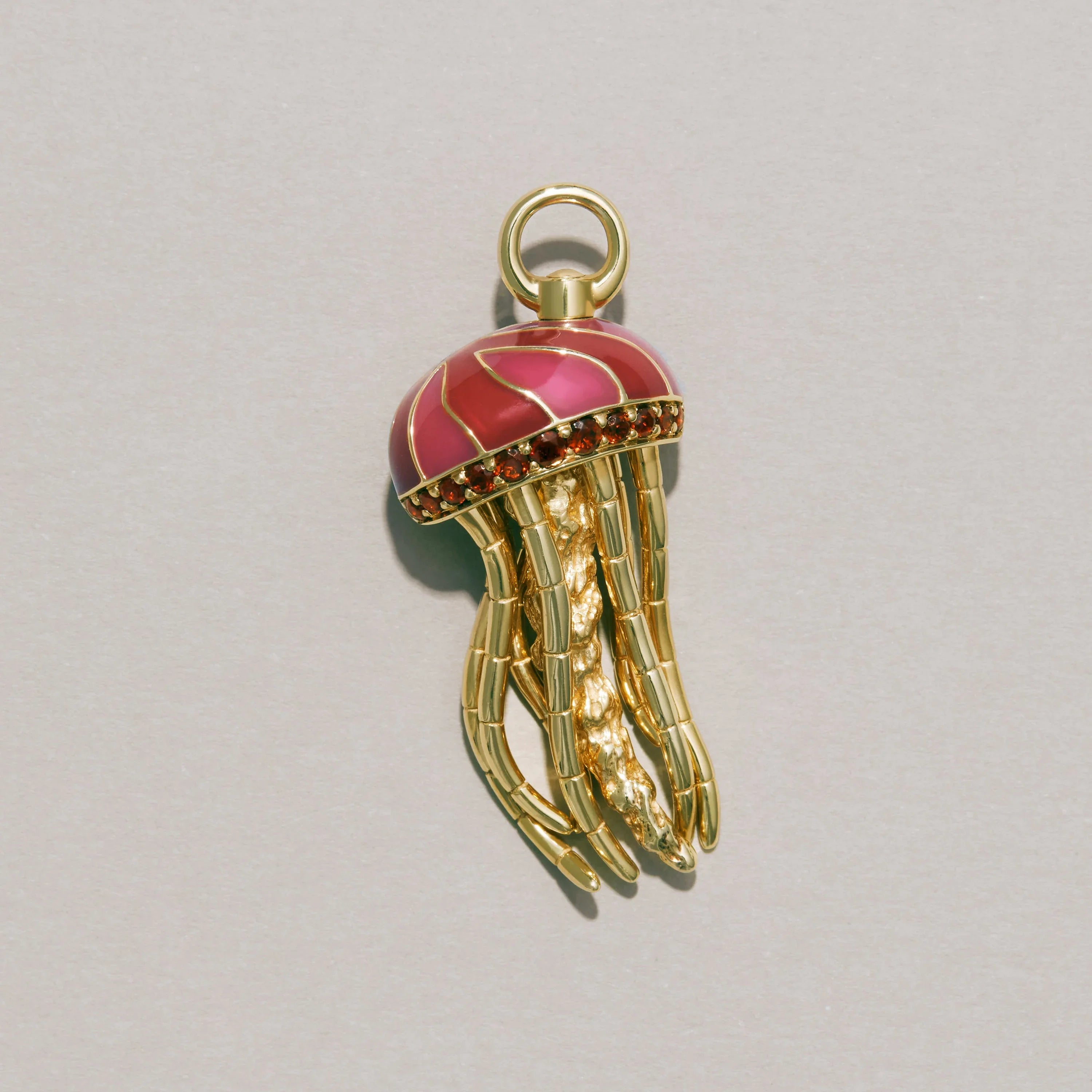 Jellyfish-shaped charm with red top and gold body on a light gray background