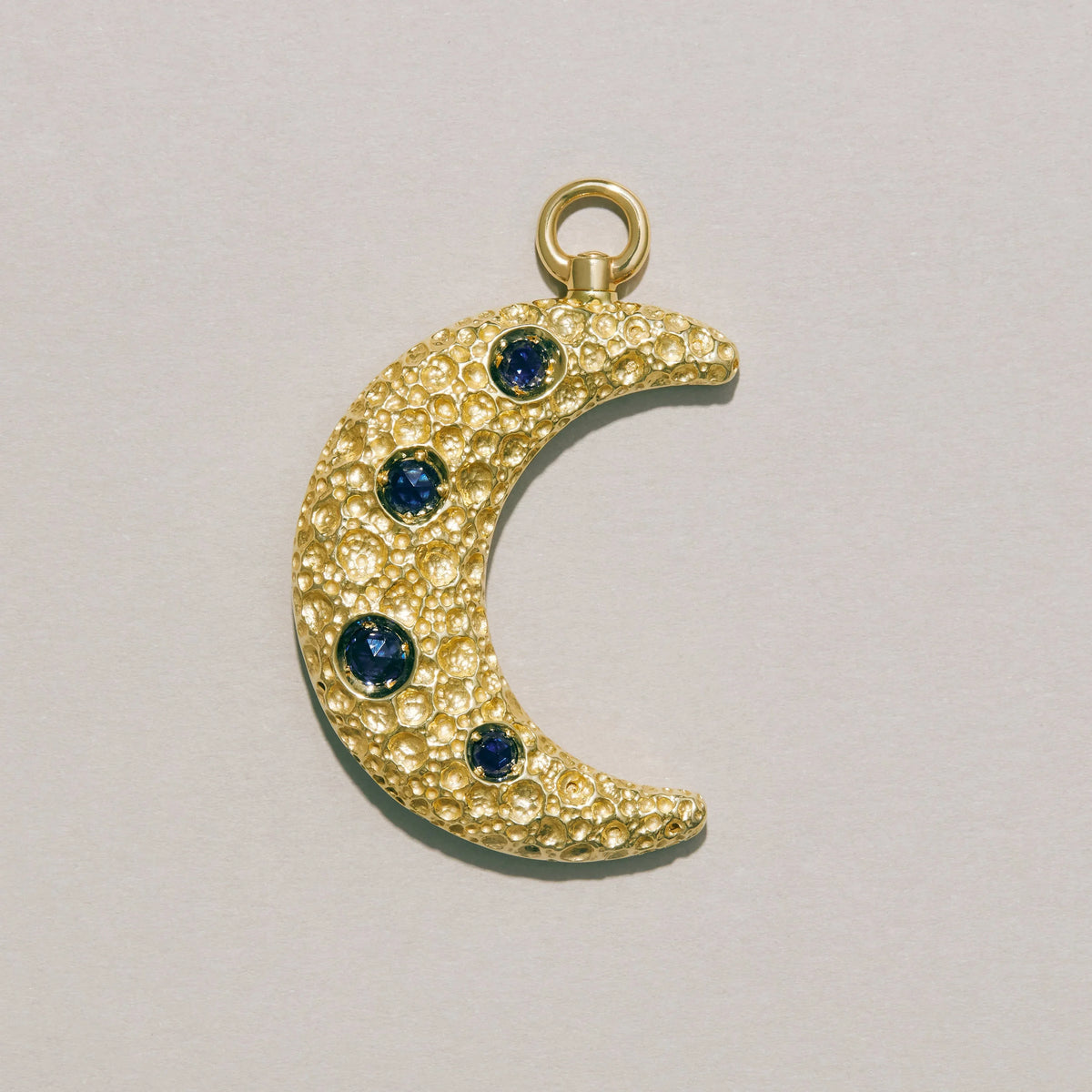Gold crescent moon charm with blue gemstones on a light gray background