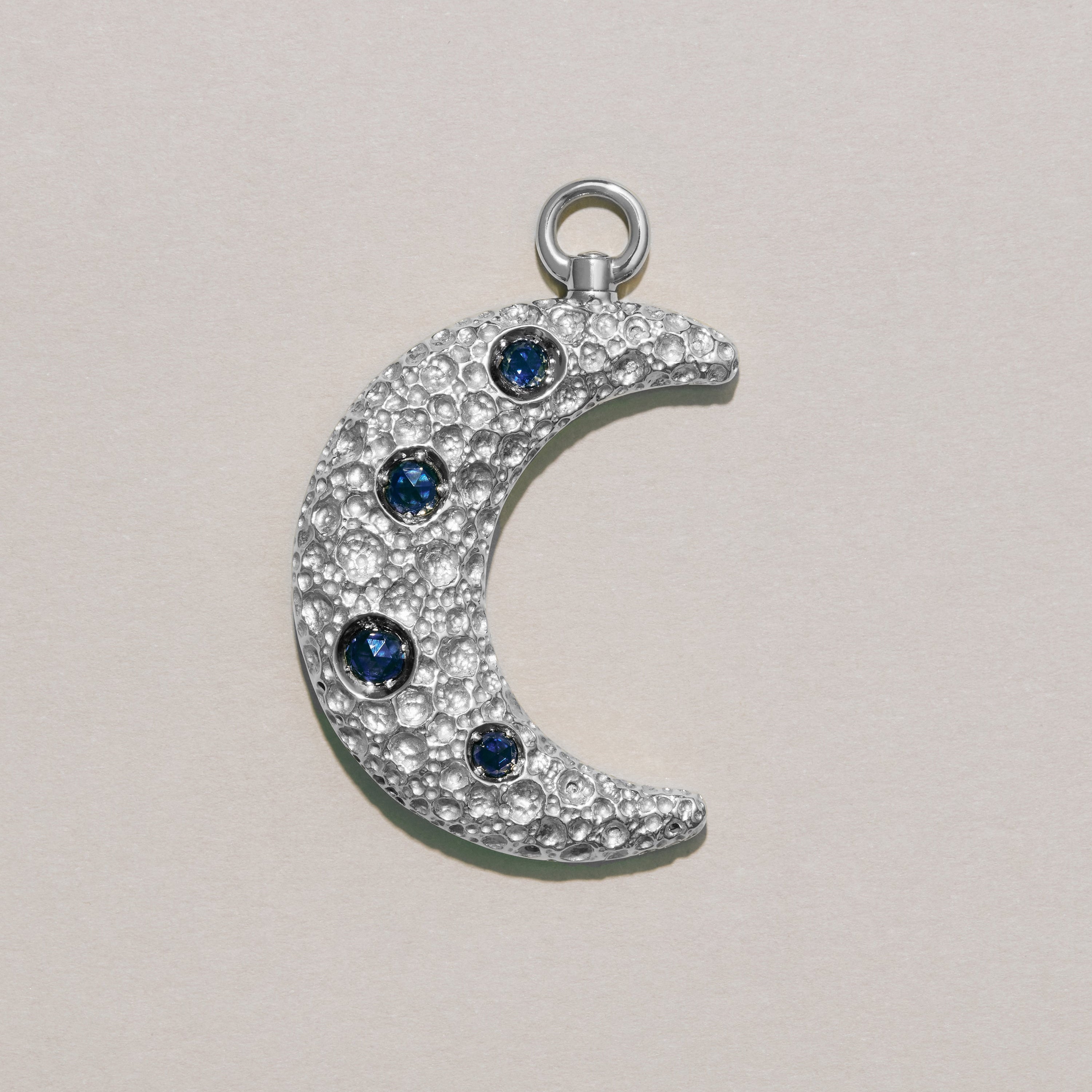 Silver crescent moon charm with blue gemstones on a light gray background