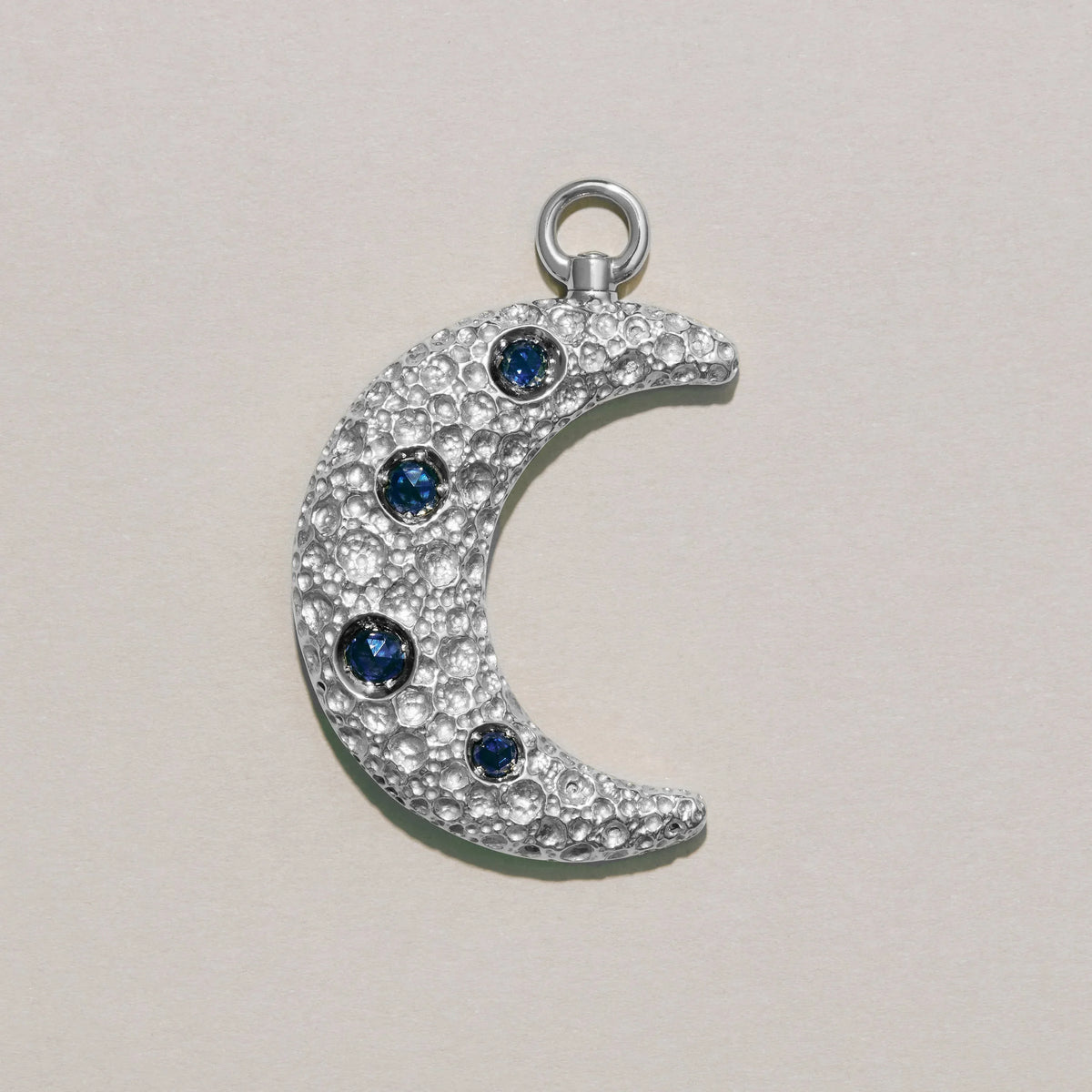Silver crescent moon charm with blue gemstones on a light gray background