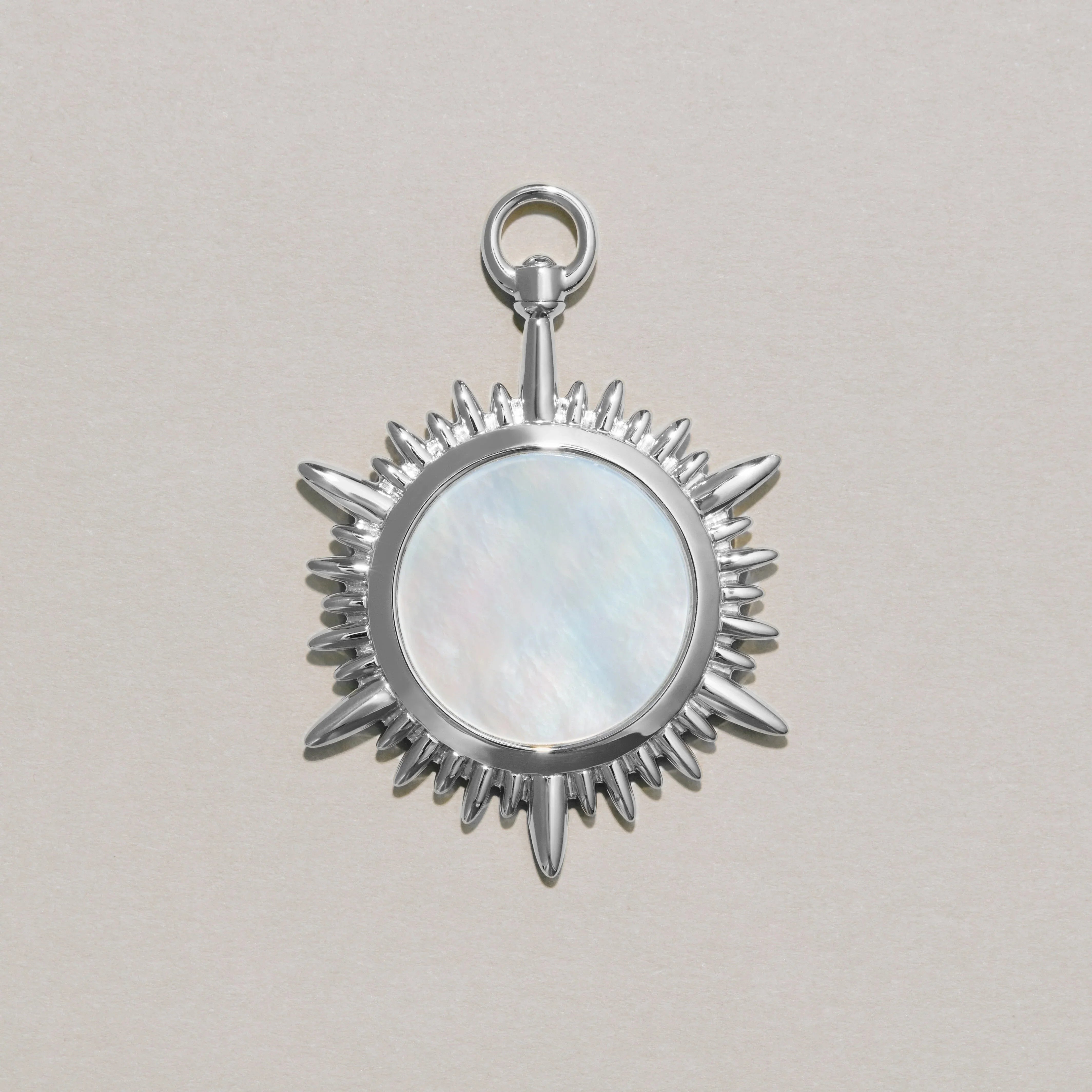 Silver sun-shaped pendant with a central circular mother-of-pearl on a light gray background