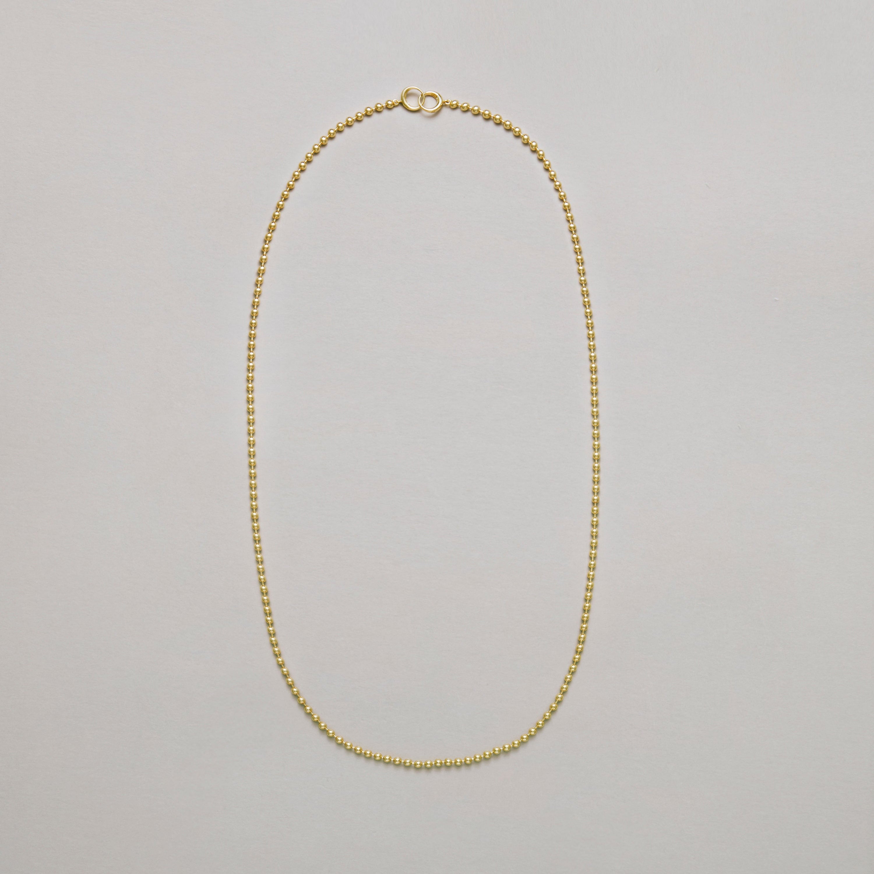 Long gold beaded chain necklace on a light gray background