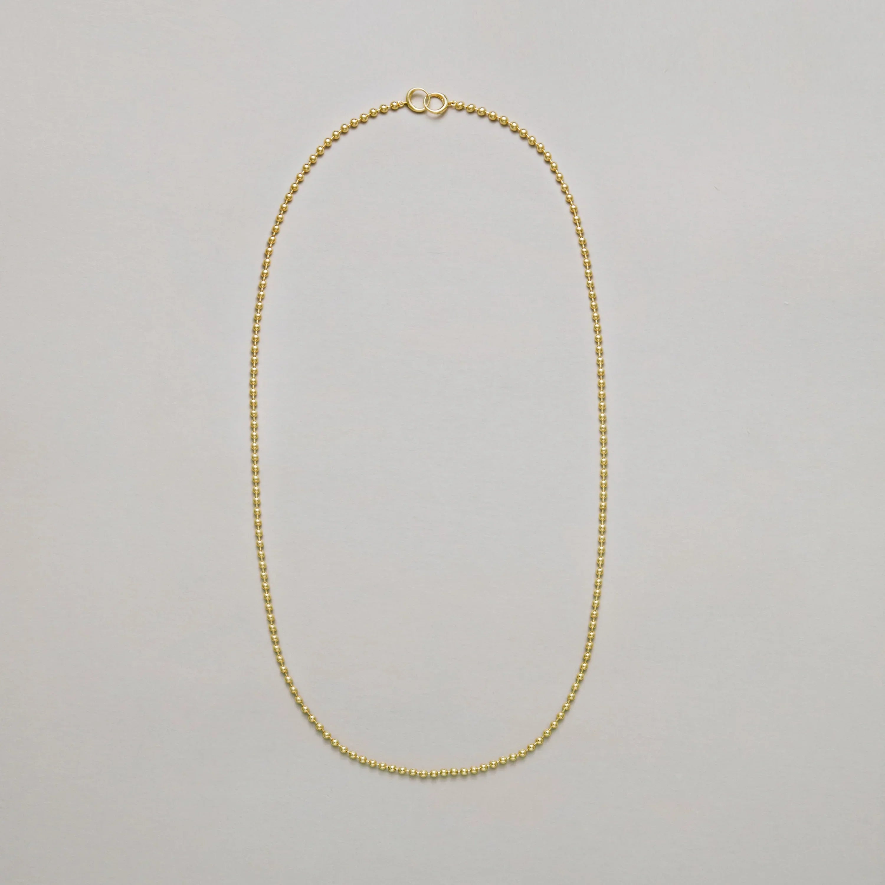 Long gold beaded chain necklace on a light gray background