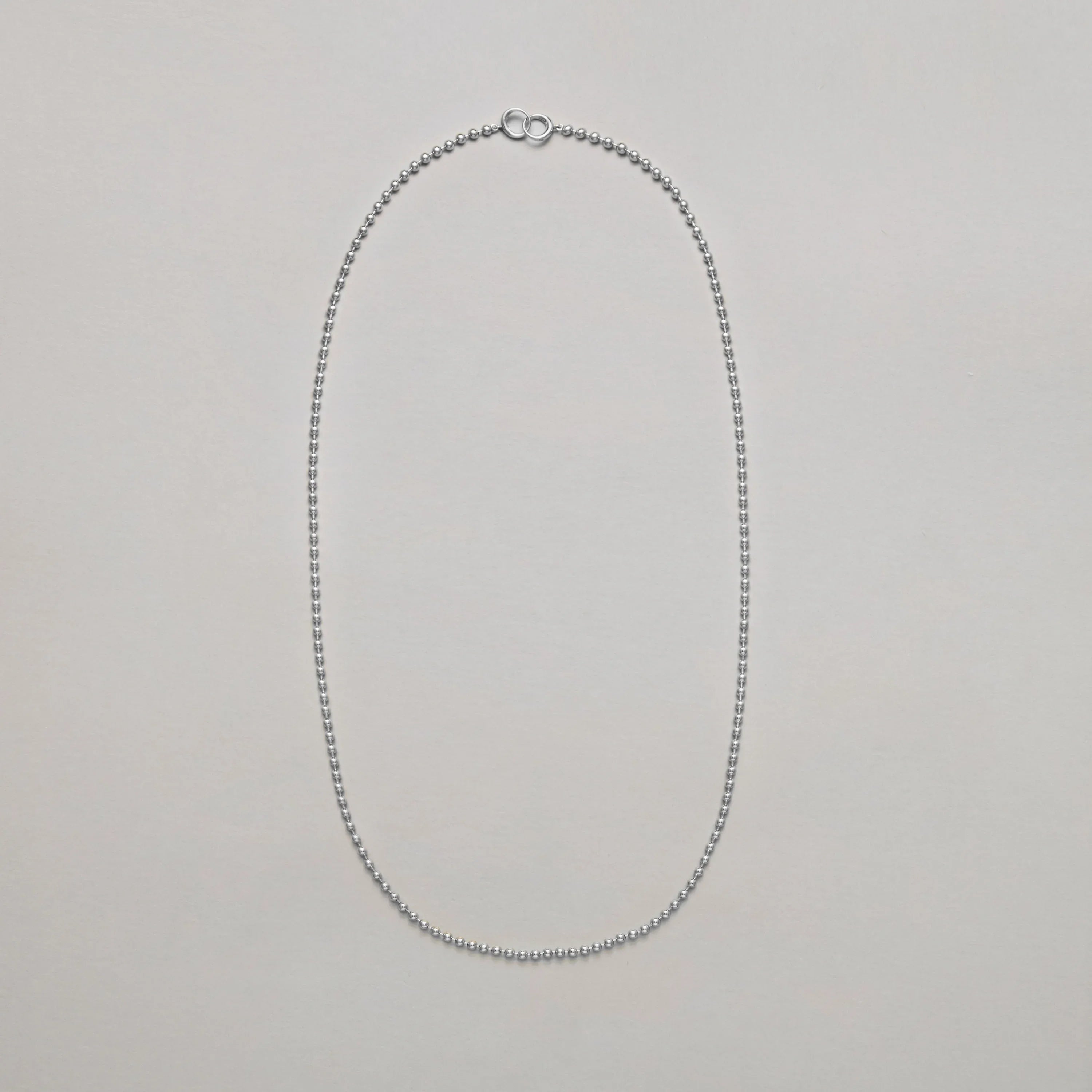 Long silver beaded chain necklace on a light gray background
