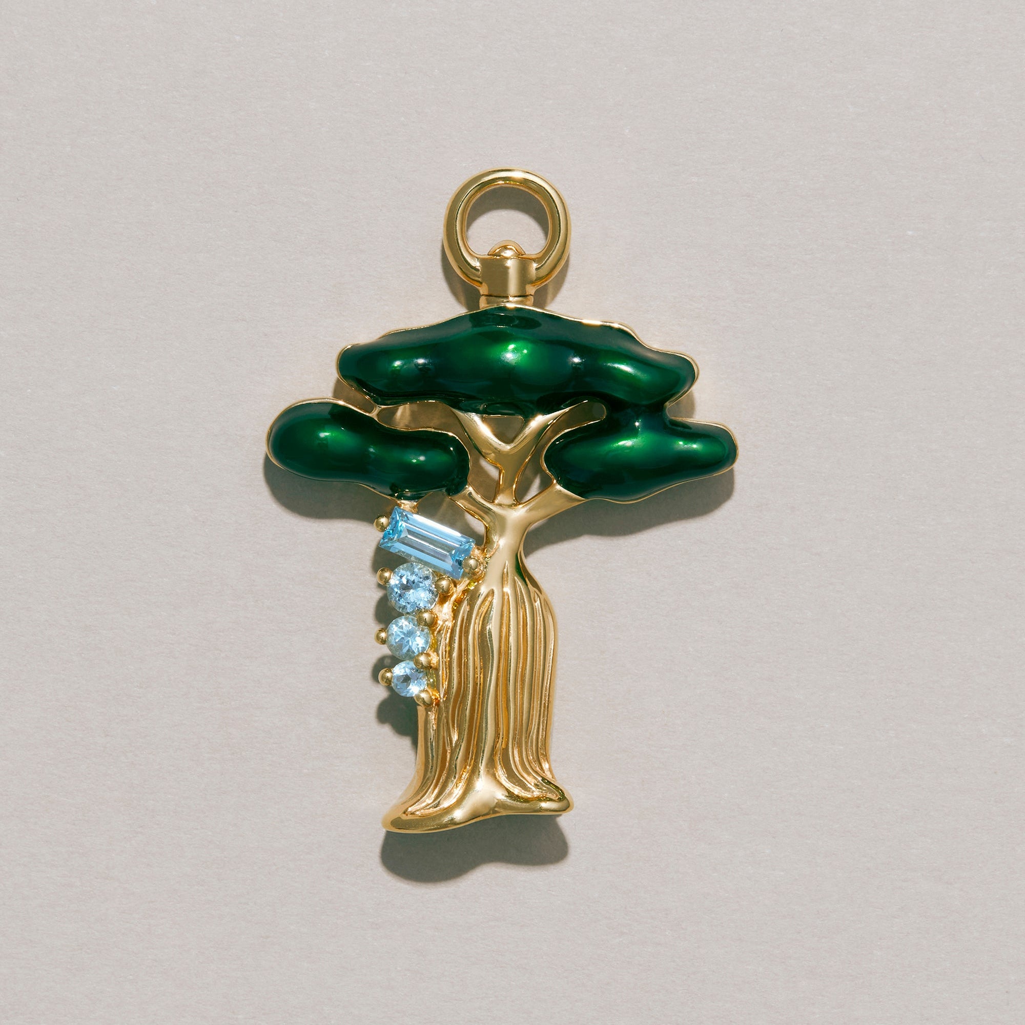 Gold pendant with green tree design and blue stones on a gray background