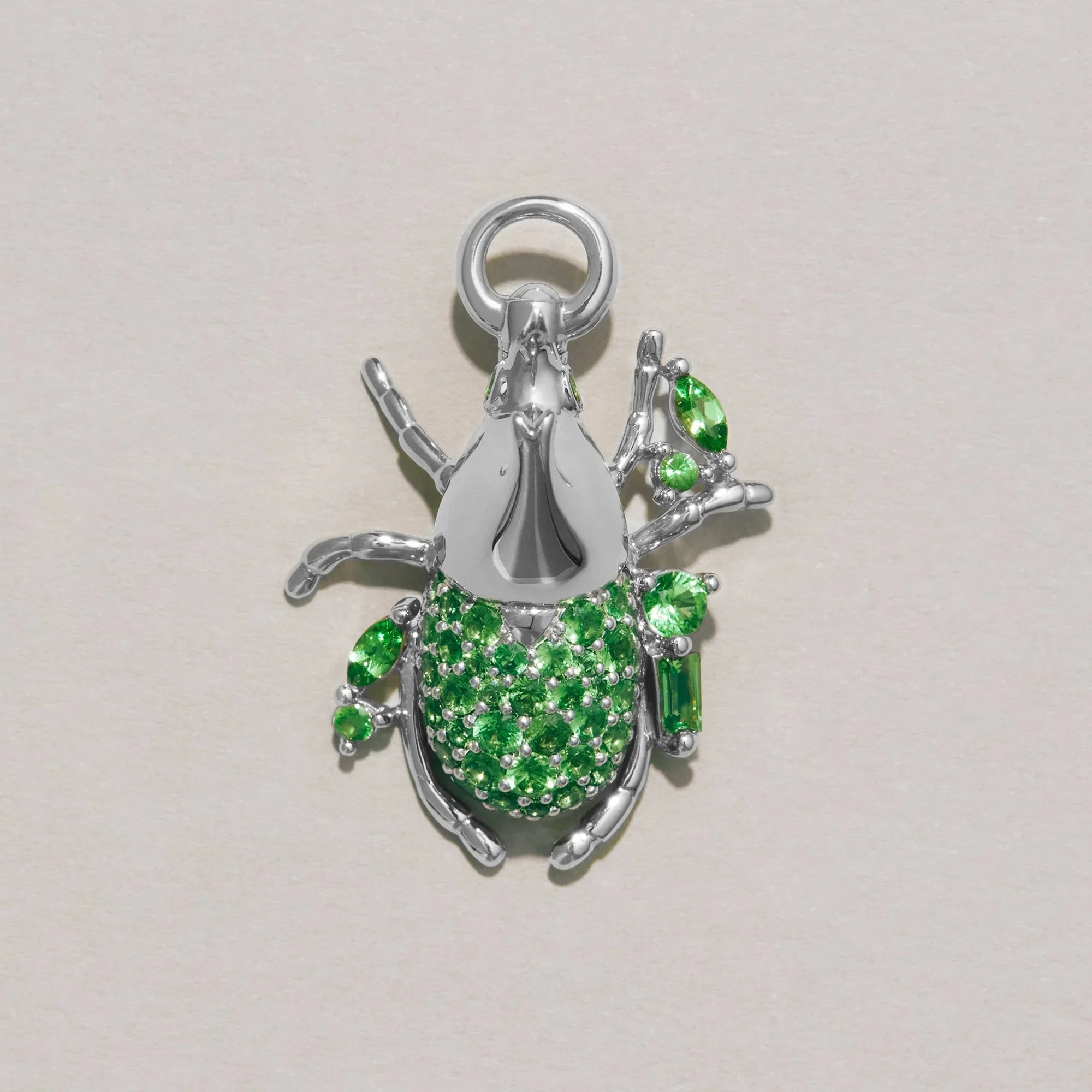 Silver beetle-shaped pendant with green gemstones on a light gray background