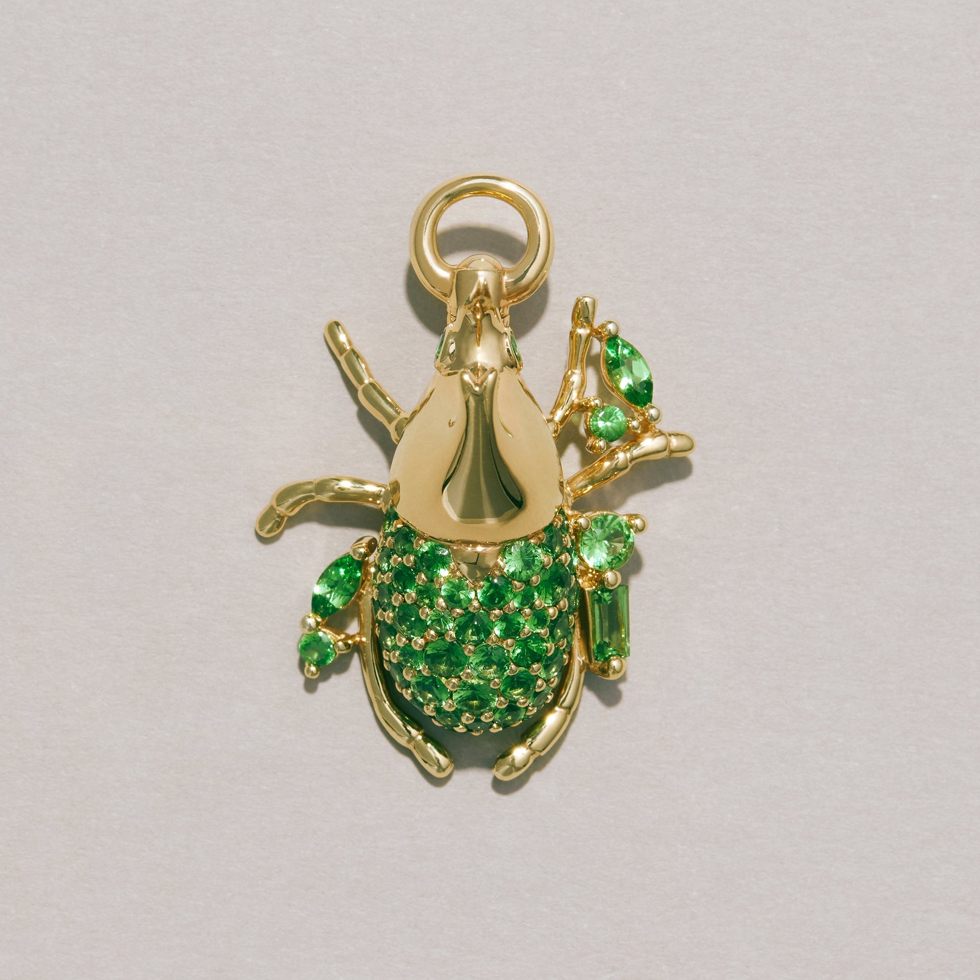 Gold beetle-shaped pendant with green gemstones on a gray background