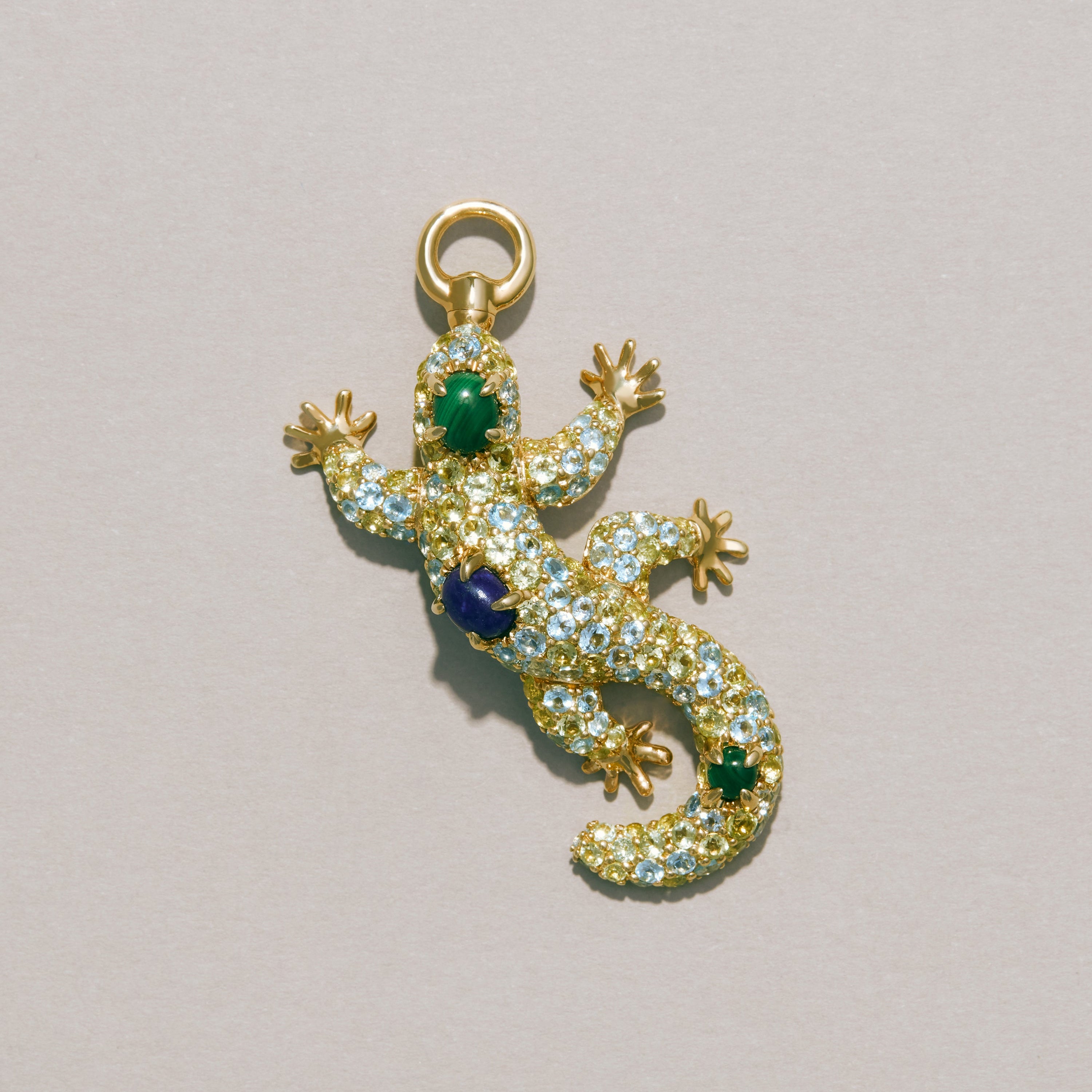 Gold lizard-shaped pendant with gemstones on a light gray background