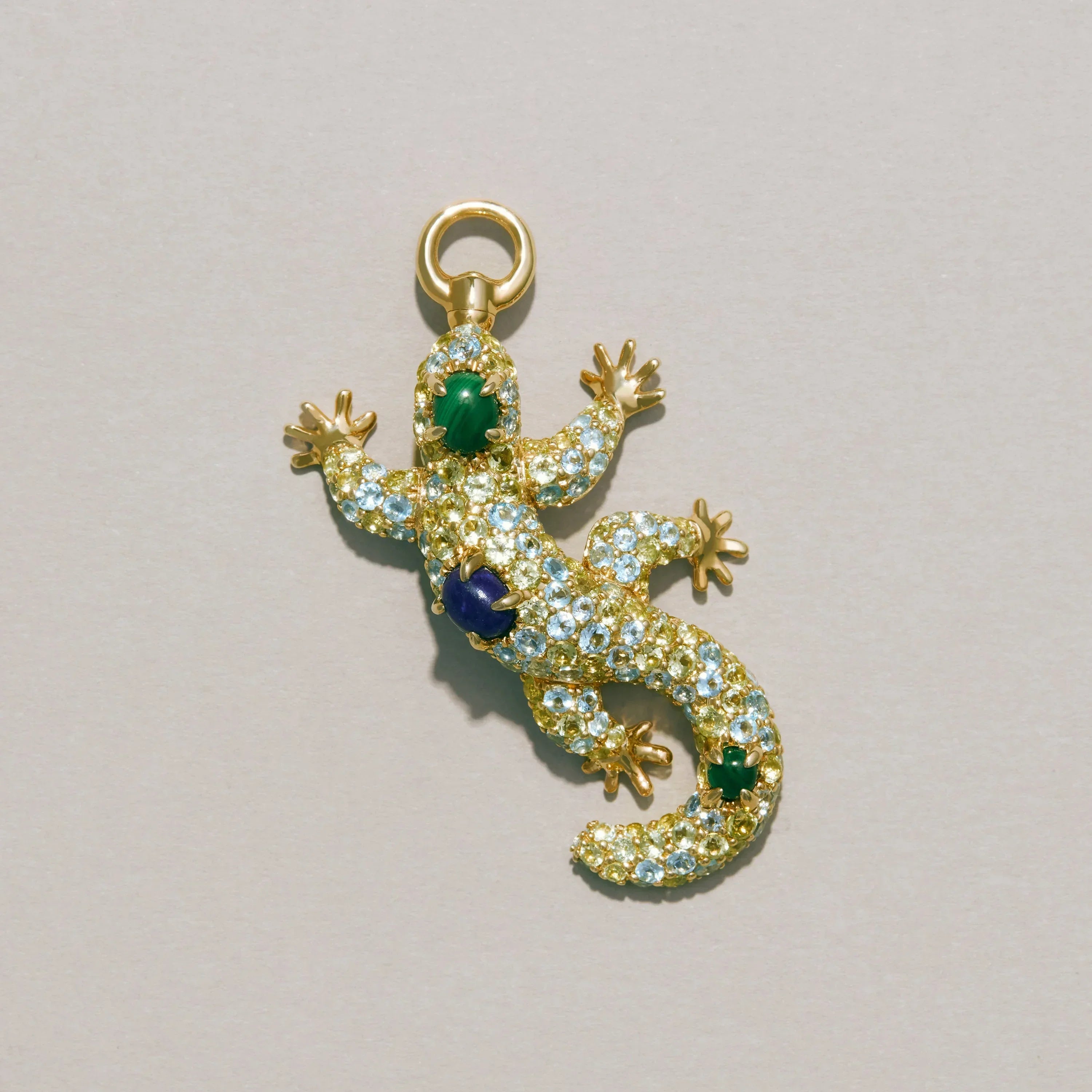 Gold lizard-shaped pendant with gemstones on a light gray background