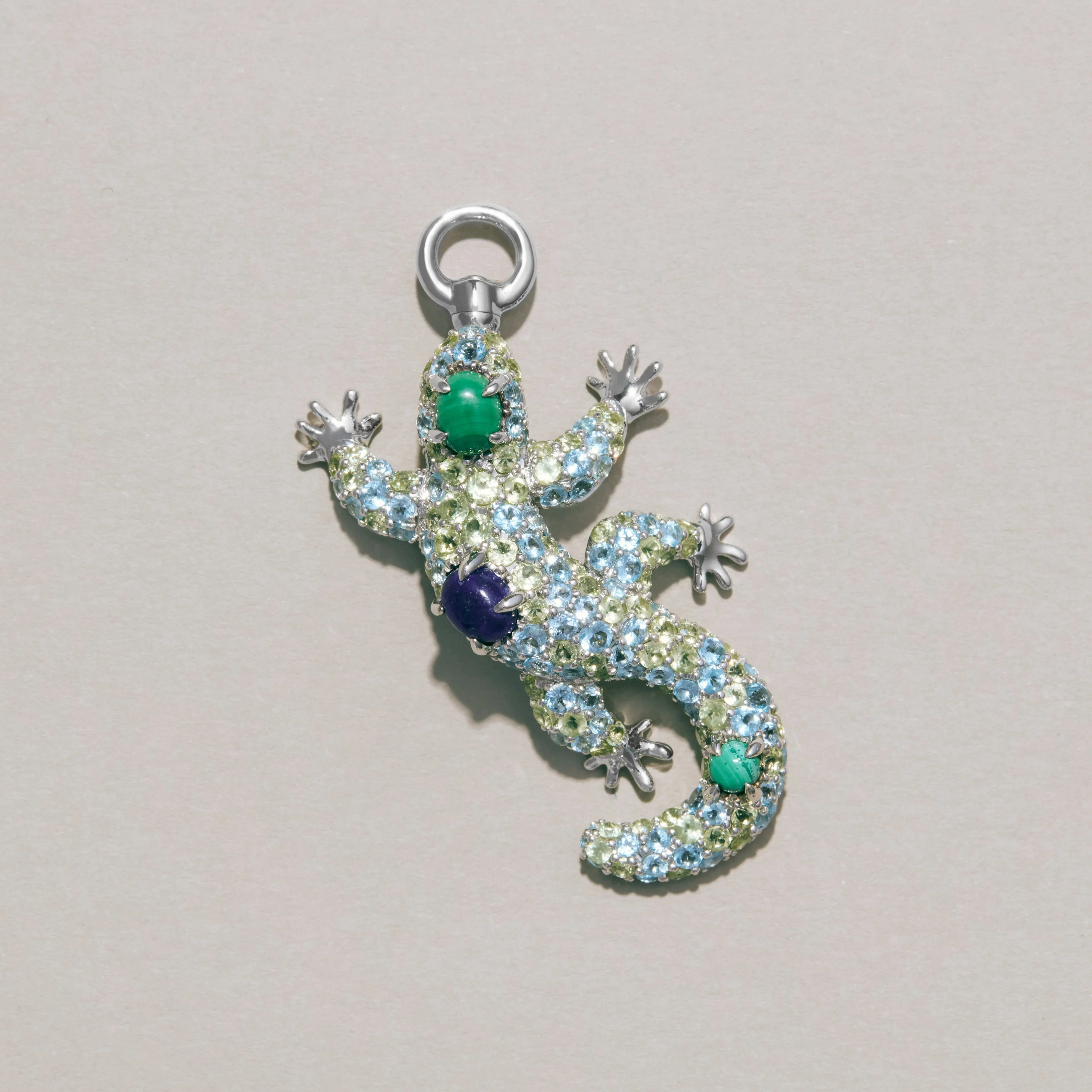 Silver gecko-shaped pendant with gemstones on a light gray background