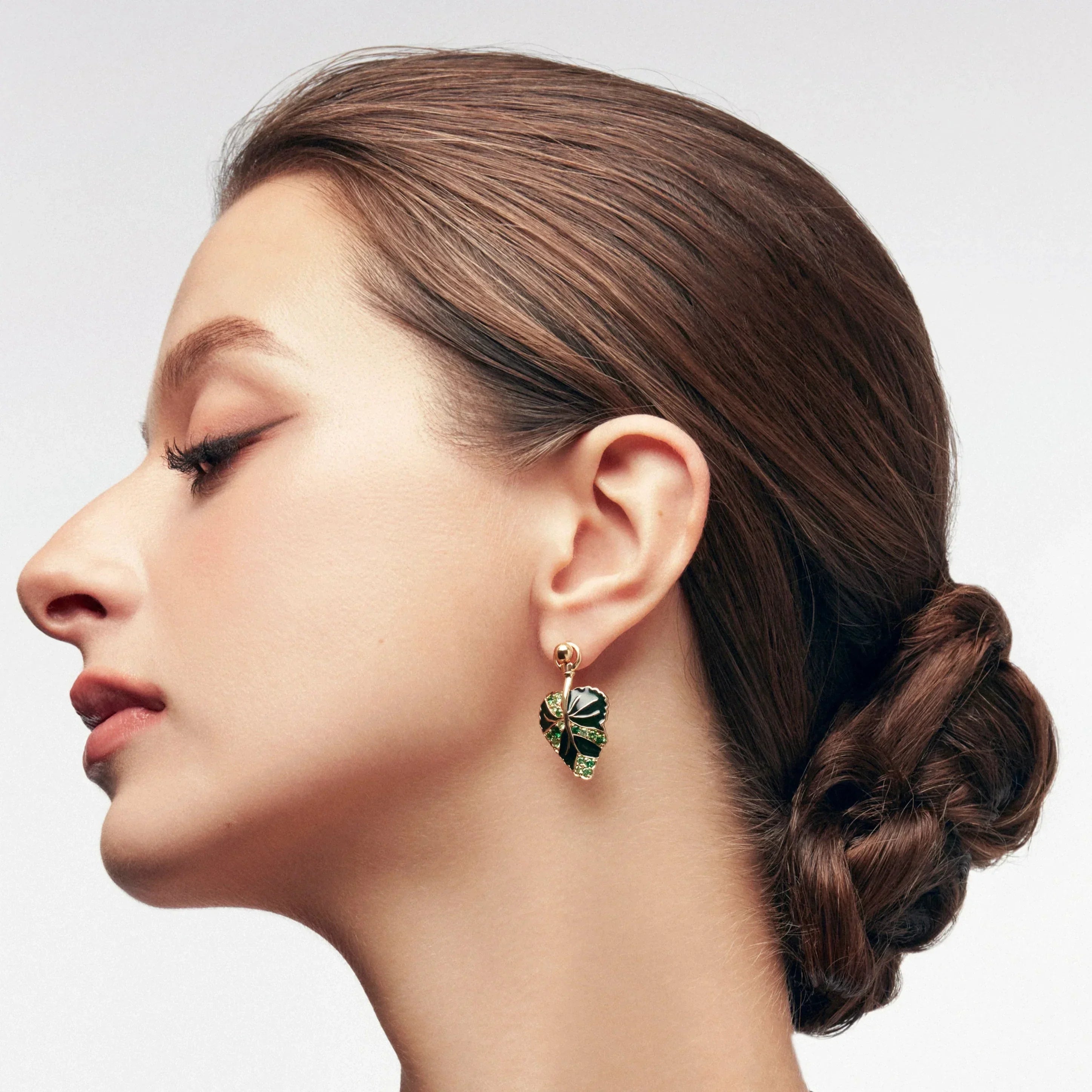 Gold stud earrings with green gemstone monstera leaf design on model