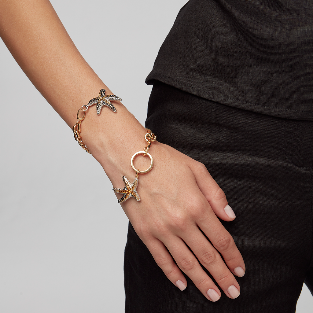 Close-up of wrist adorned with gold bracelet featuring two jeweled starfish charms.