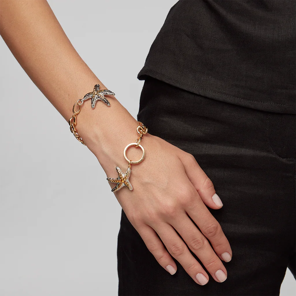 Close-up of wrist adorned with gold bracelet featuring two jeweled starfish charms.