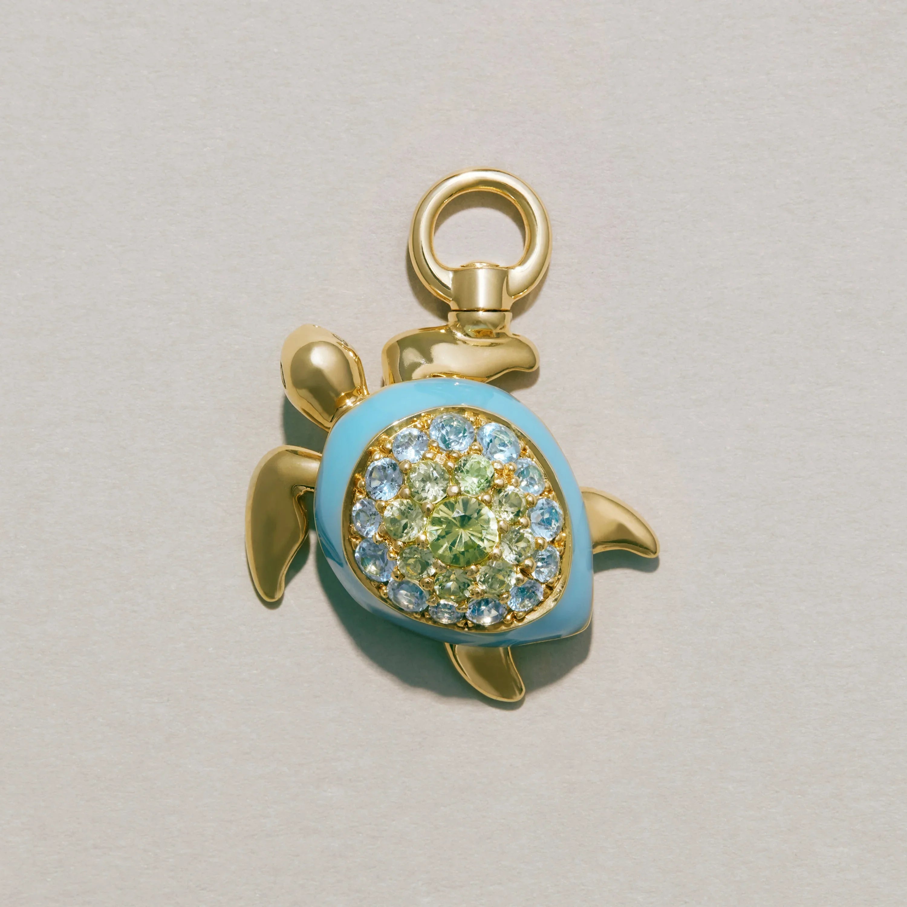 Gold turtle-shaped pendant with blue and green gemstones on a light gray background