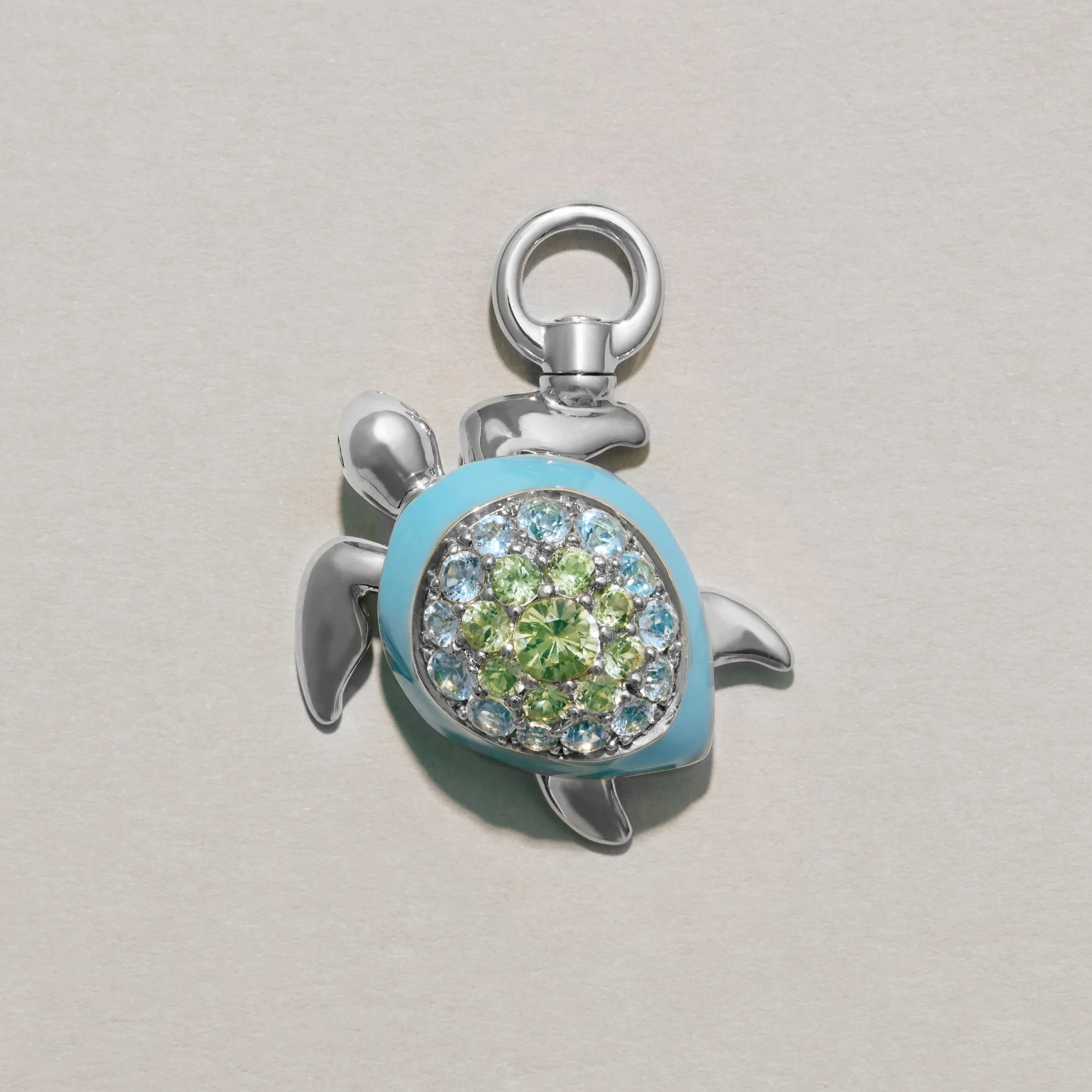 Silver turtle-shaped charm with blue and green gemstones on a light gray background