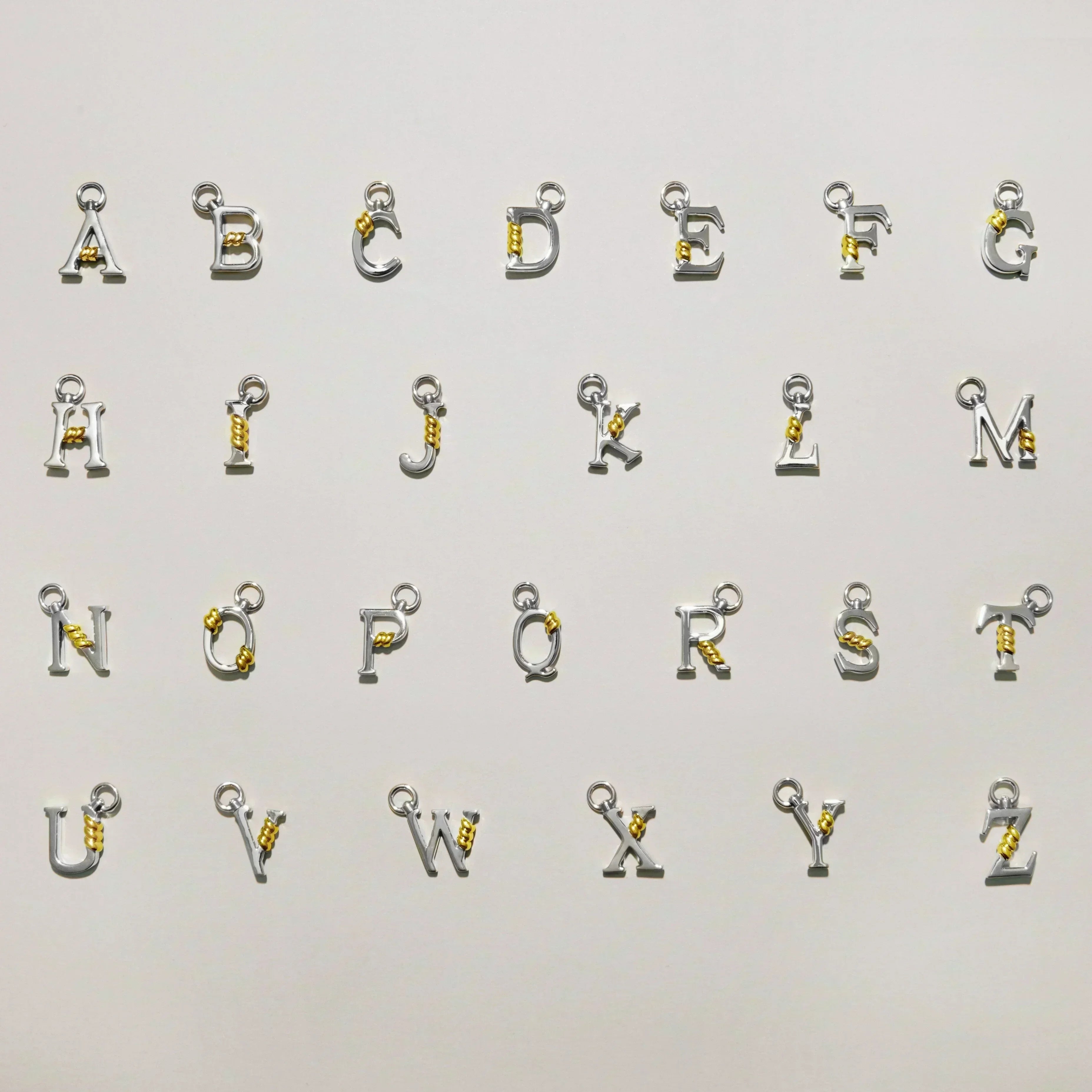 Full A to Z collection of silver letter charms each featuring a gold rope twist detail, arranged on a light background.