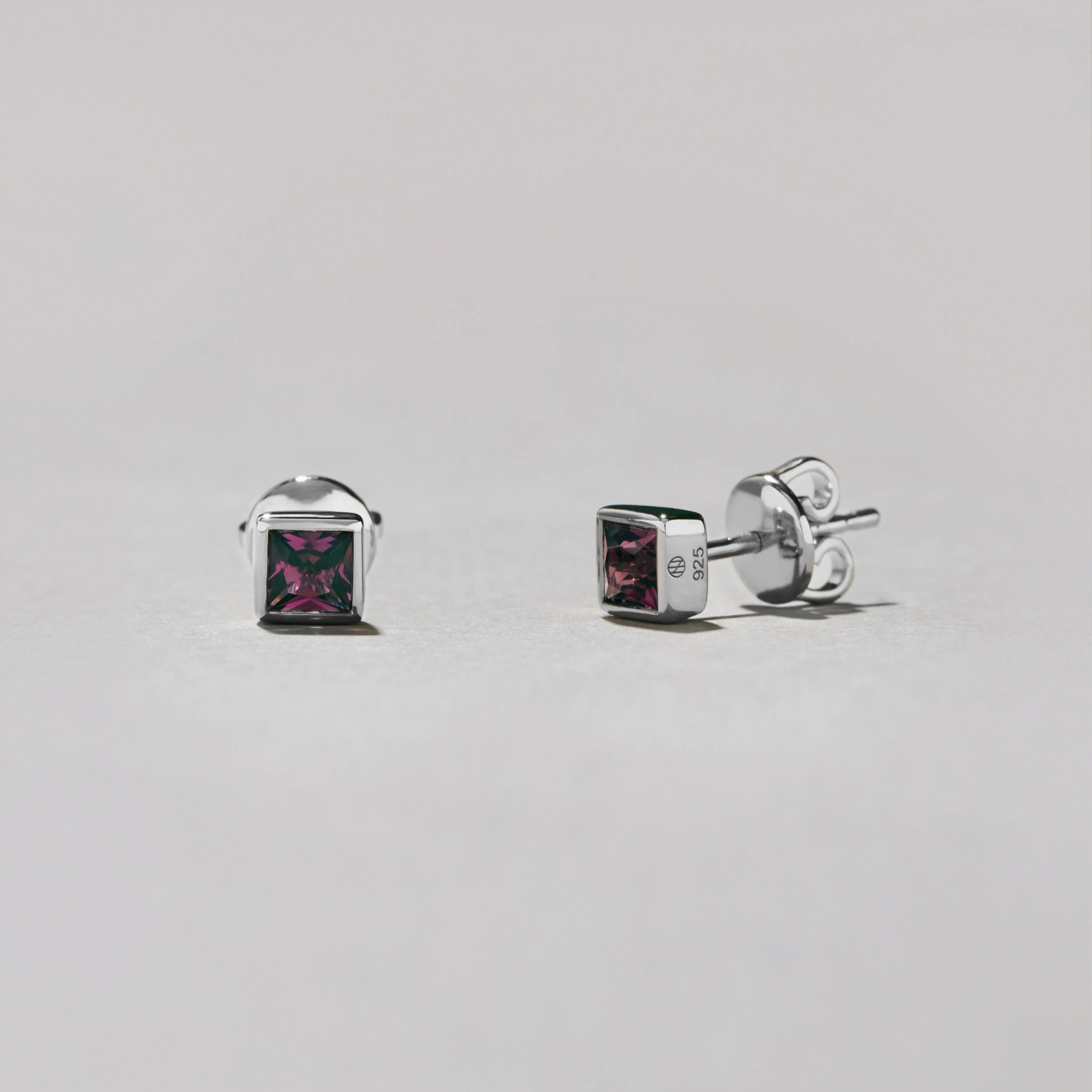 Pair of silver square stud earrings with gemstones on a light gray background