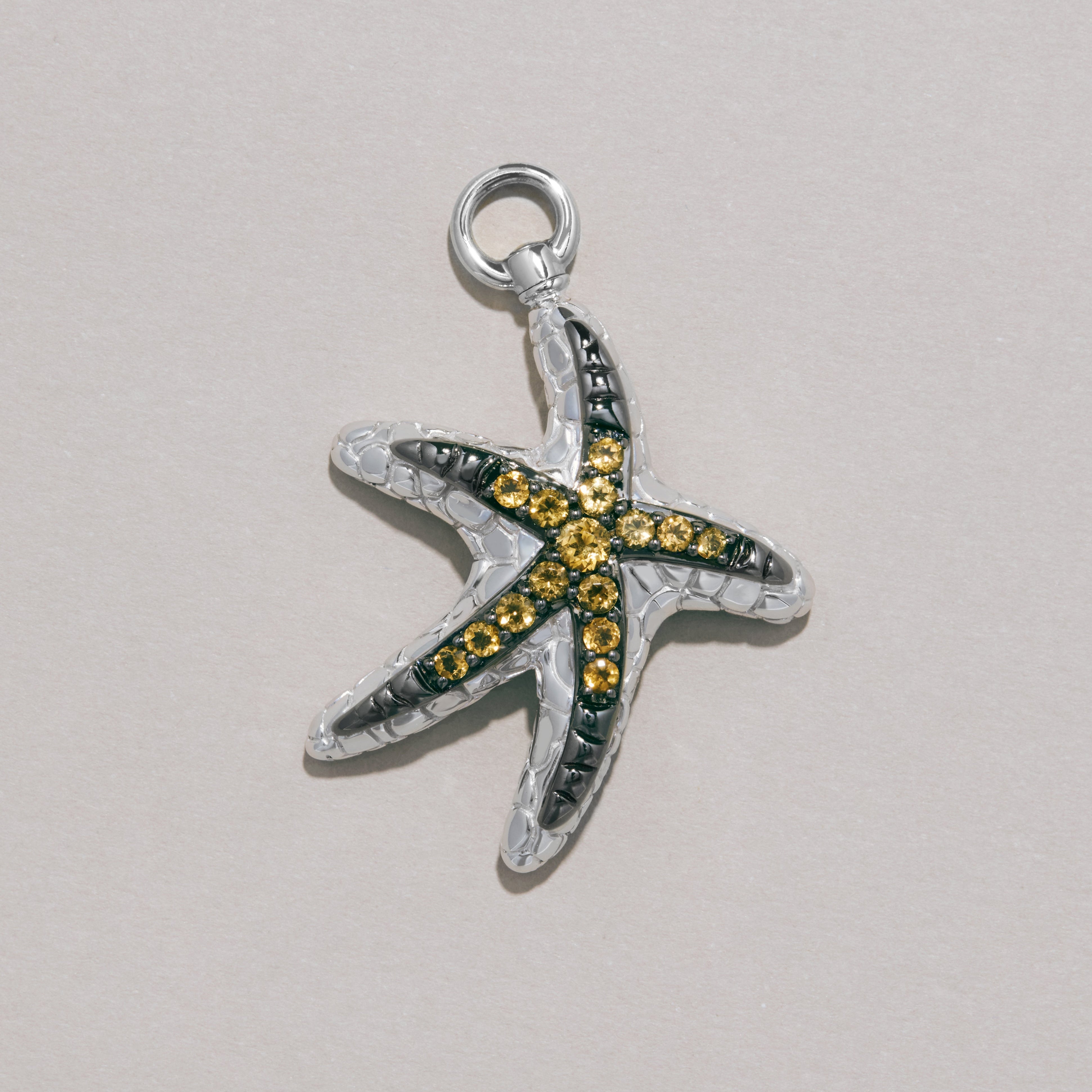 Silver starfish charm with yellow gemstones on textured background.