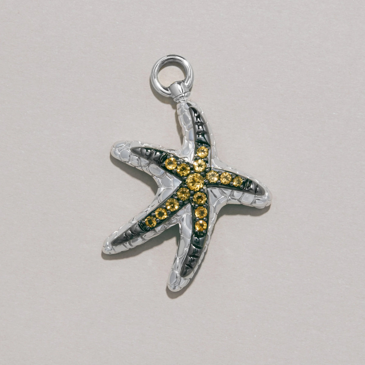 Silver starfish charm with yellow gemstones on textured background.