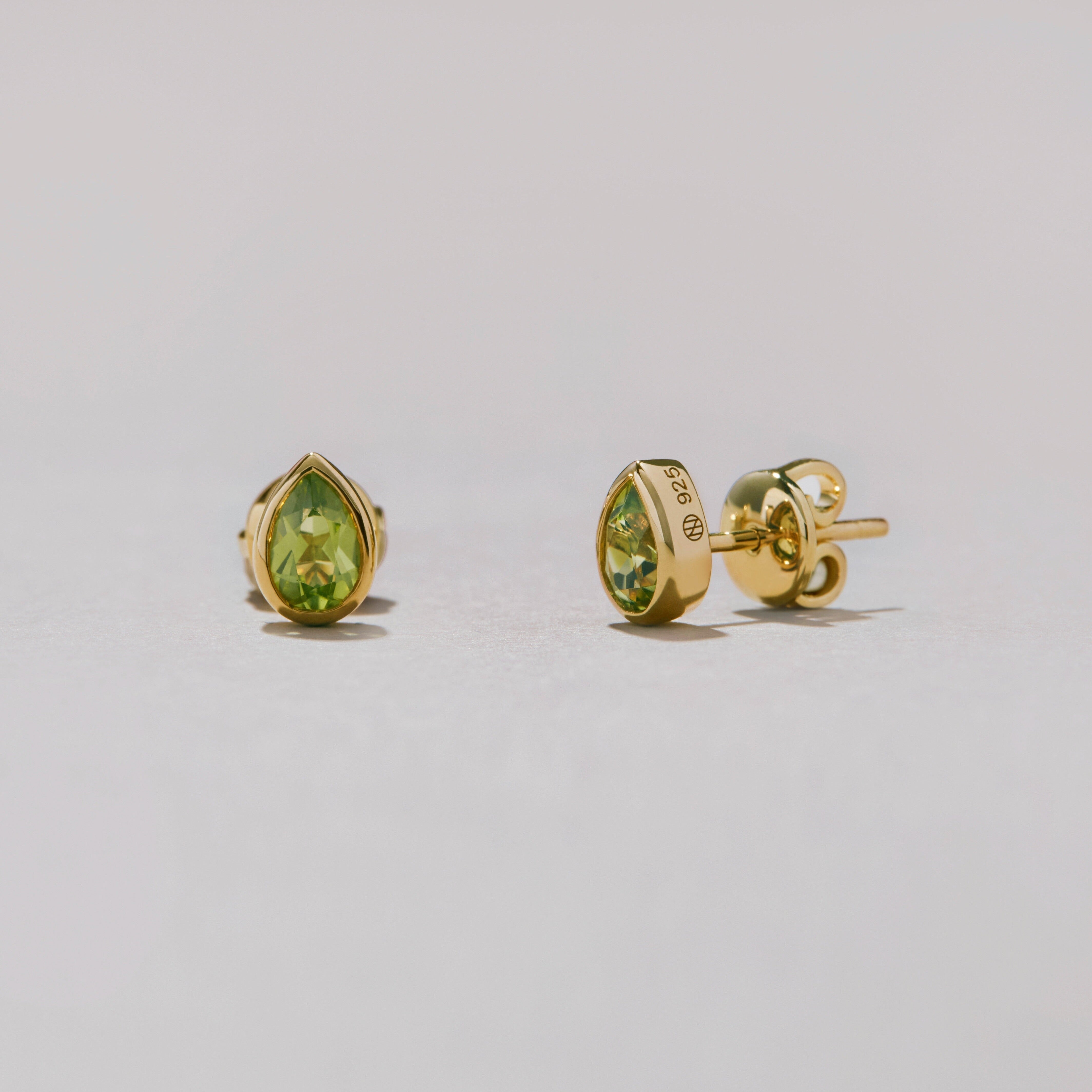 Pear-shaped gold earrings with green gemstones on a light gray background