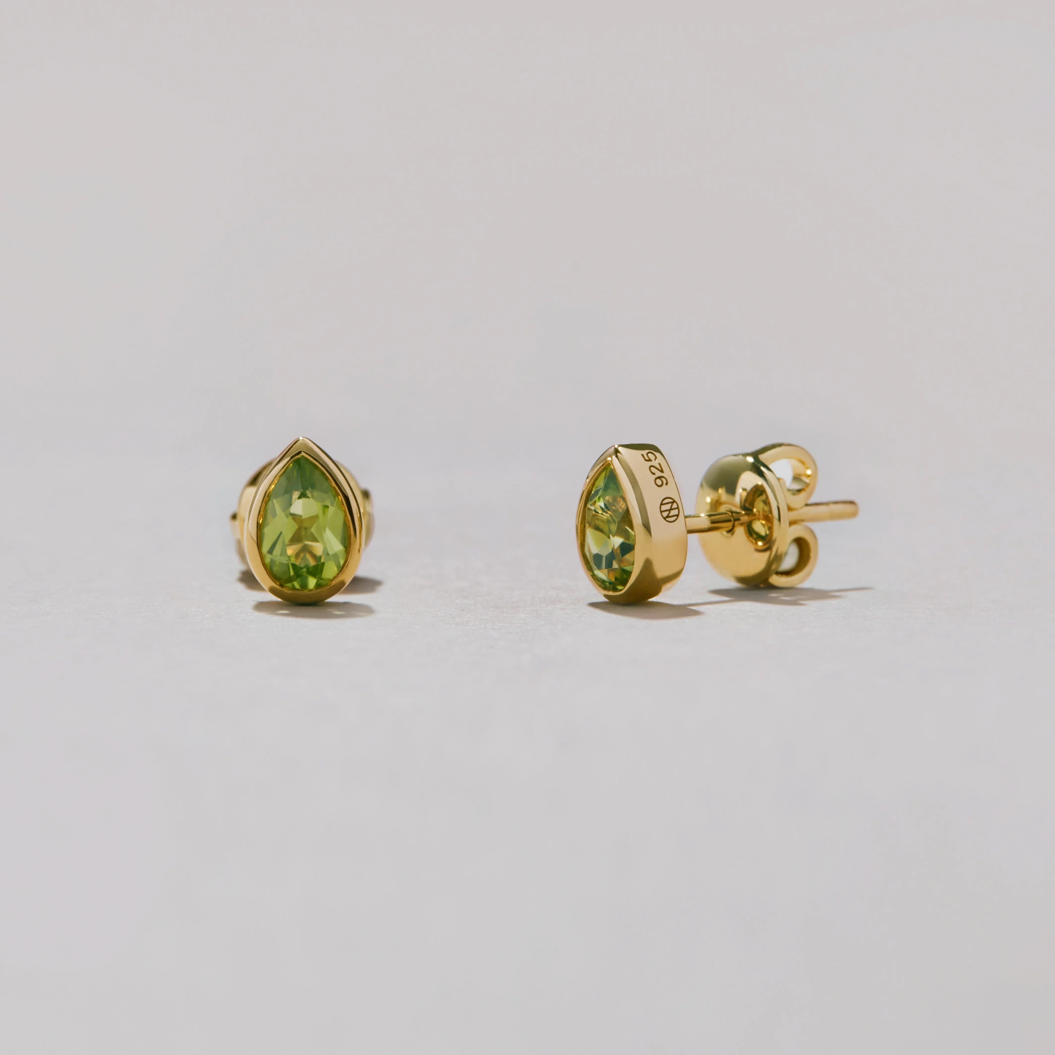 Pear-shaped gold earrings with green gemstones on a light gray background